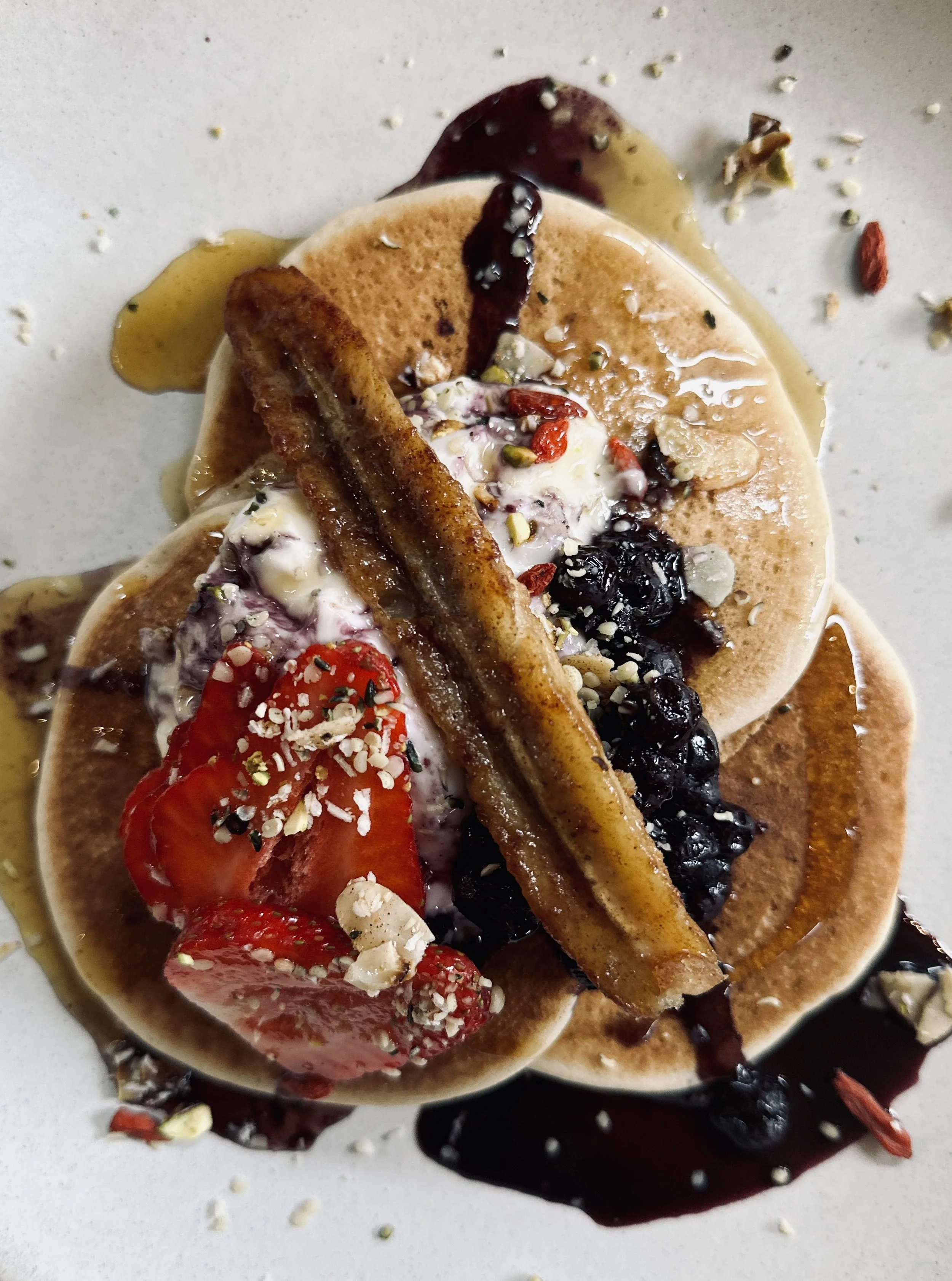 Close-up of two pancakes topped with strawberries, blueberries, whipped cream, chocolate syrup, and chopped nuts.