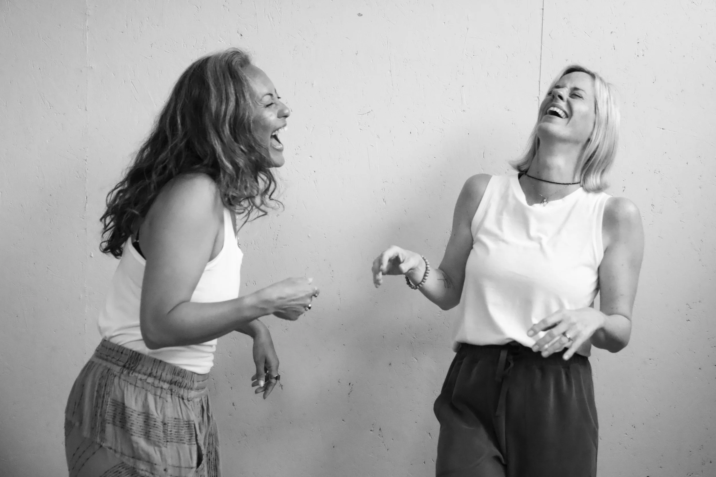 Two women laughing and enjoying each other's company in front of a plain wall.