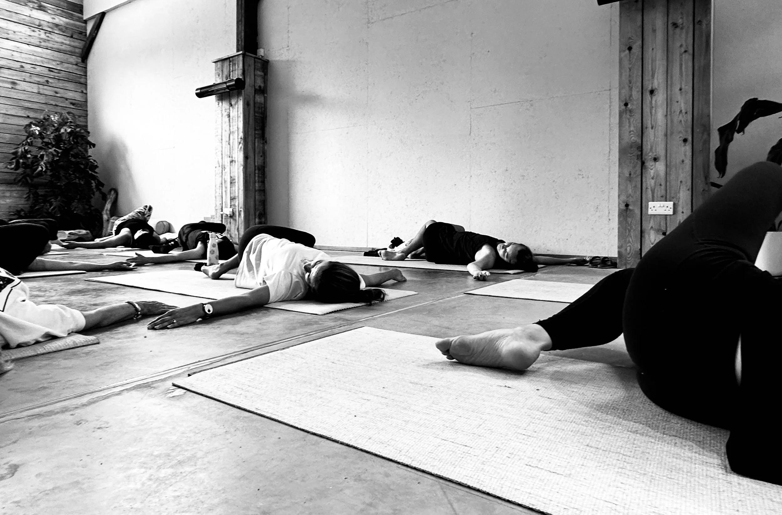 People participating in a yoga class, lying on yoga mats in a spacious, minimalistic studio.