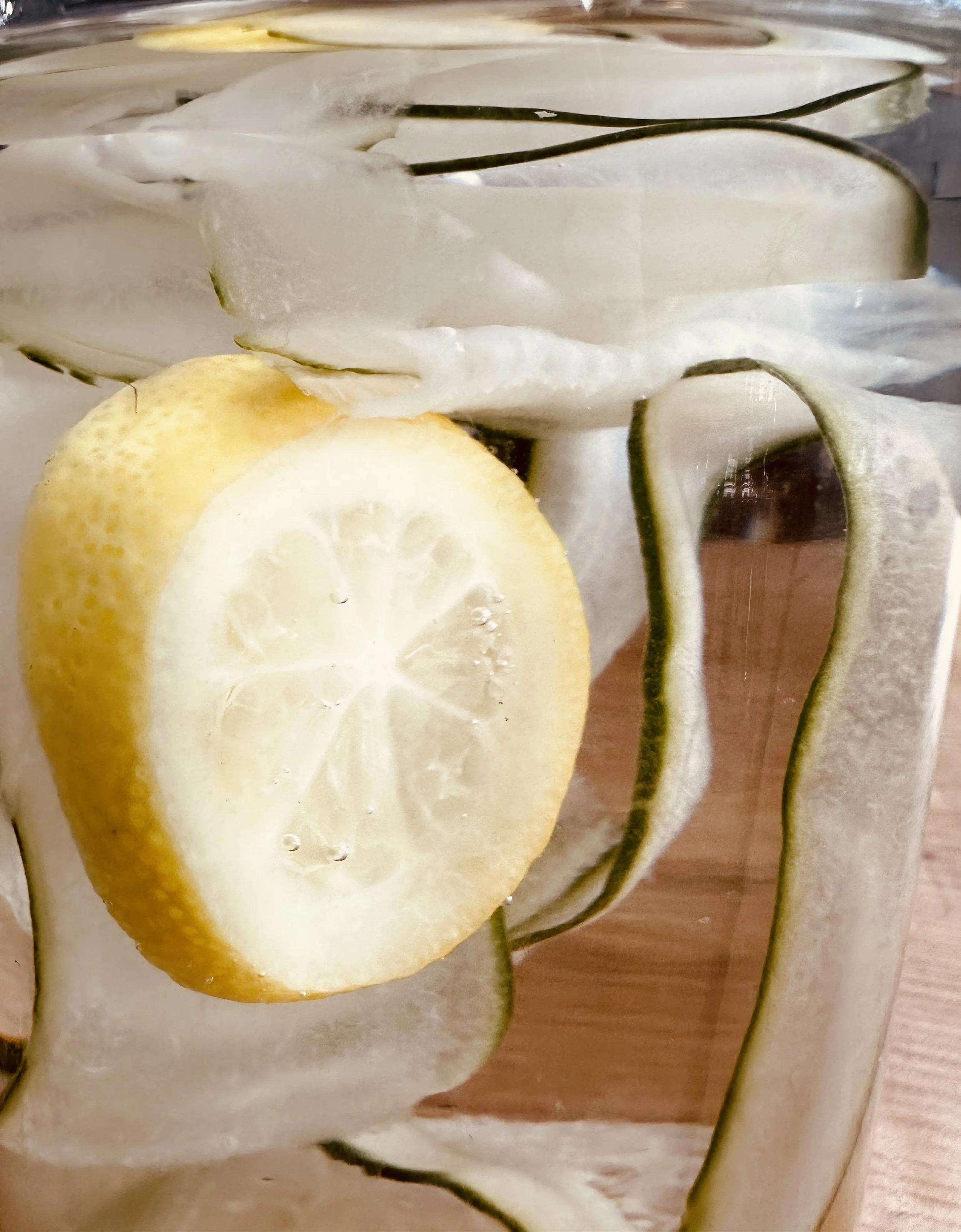 Close-up of a glass with lemon slices and cucumber slices inside.