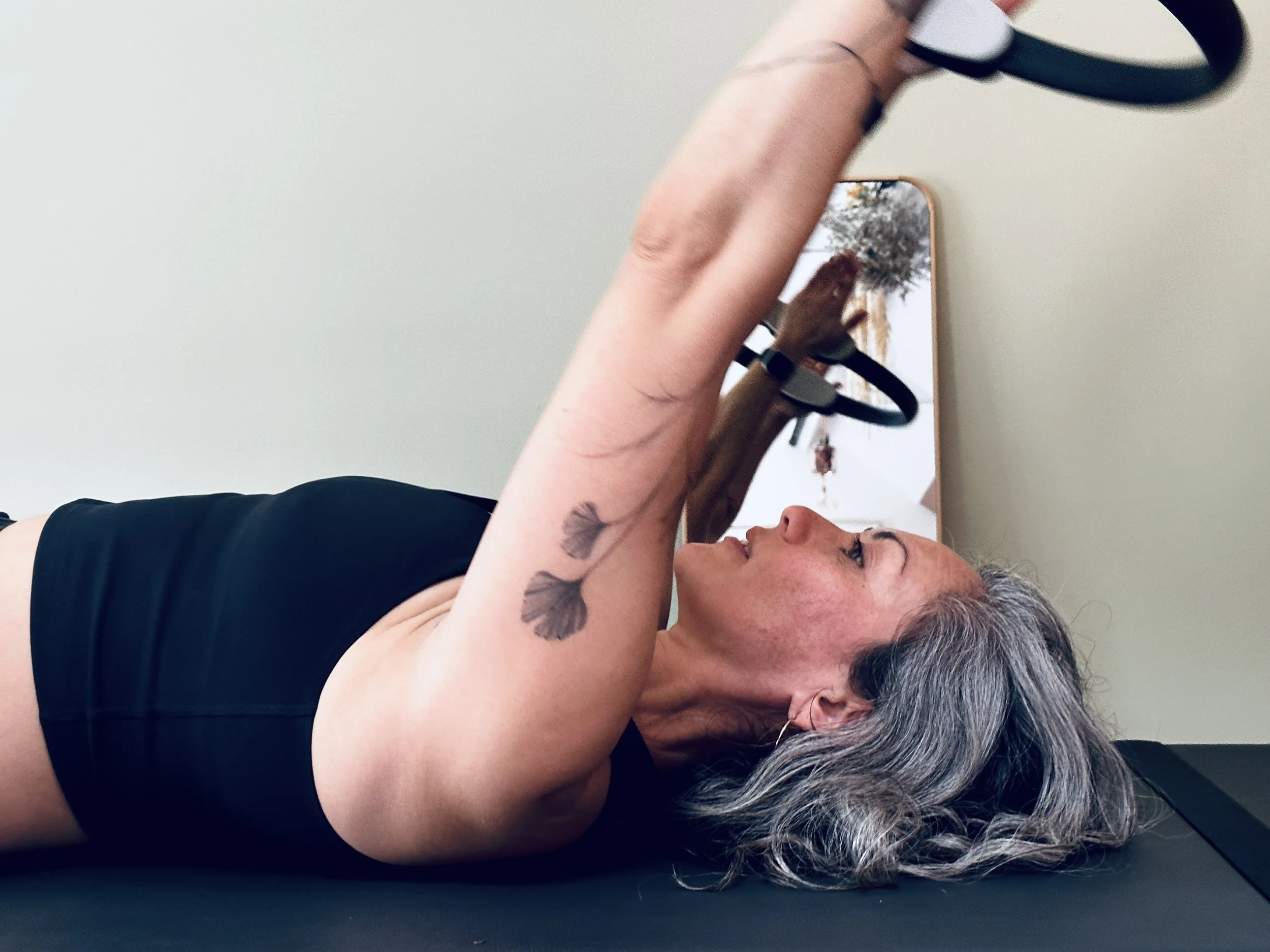 Woman lying on her back on an exercise mat, holding a pair of weights above her chest during a workout.