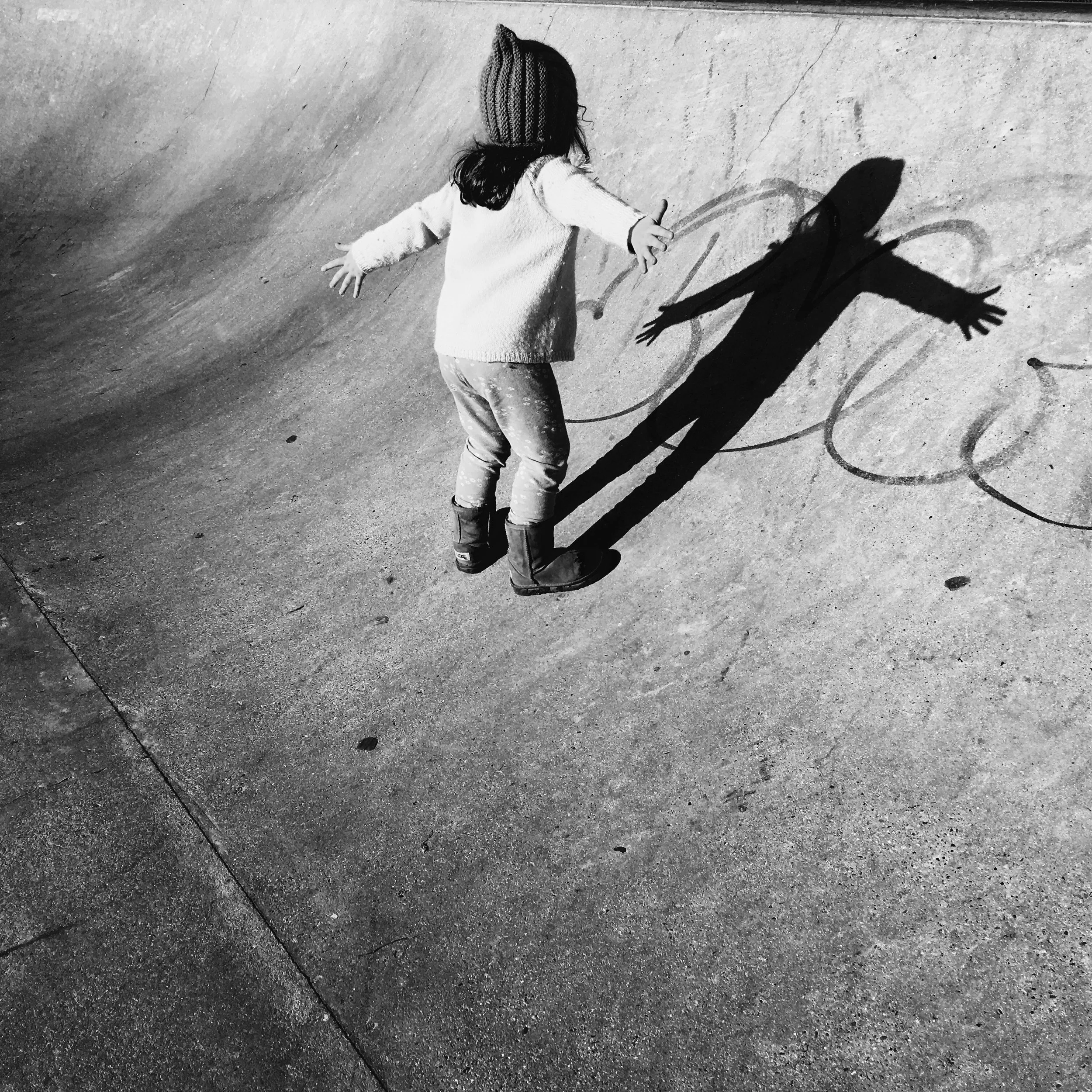 A girl drawing on the ground with her shadow cast on the pavement.