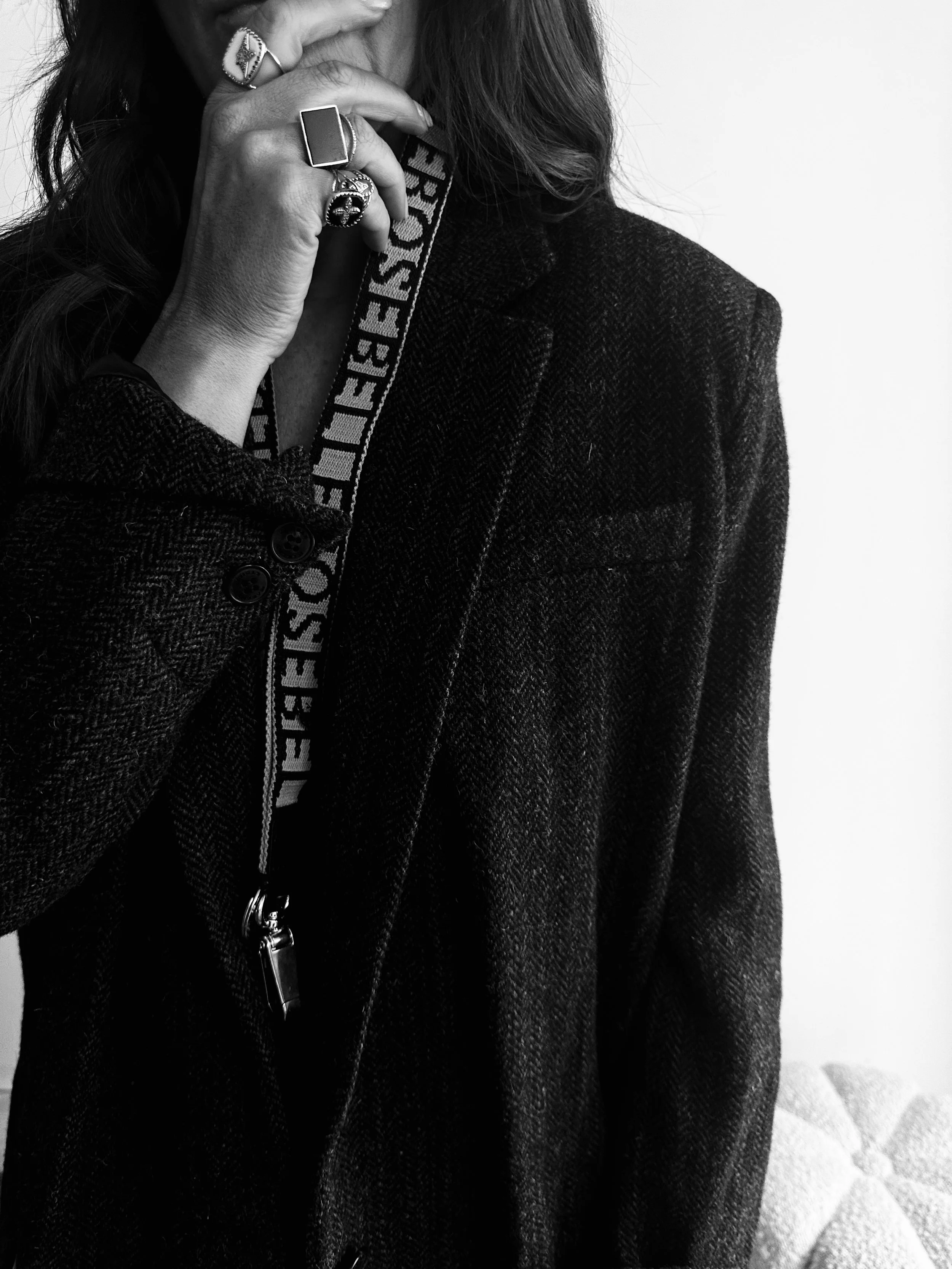 Close-up of a woman wearing a dark blazer, holding her face with her hand adorned with multiple rings, and wearing a lanyard around her neck.