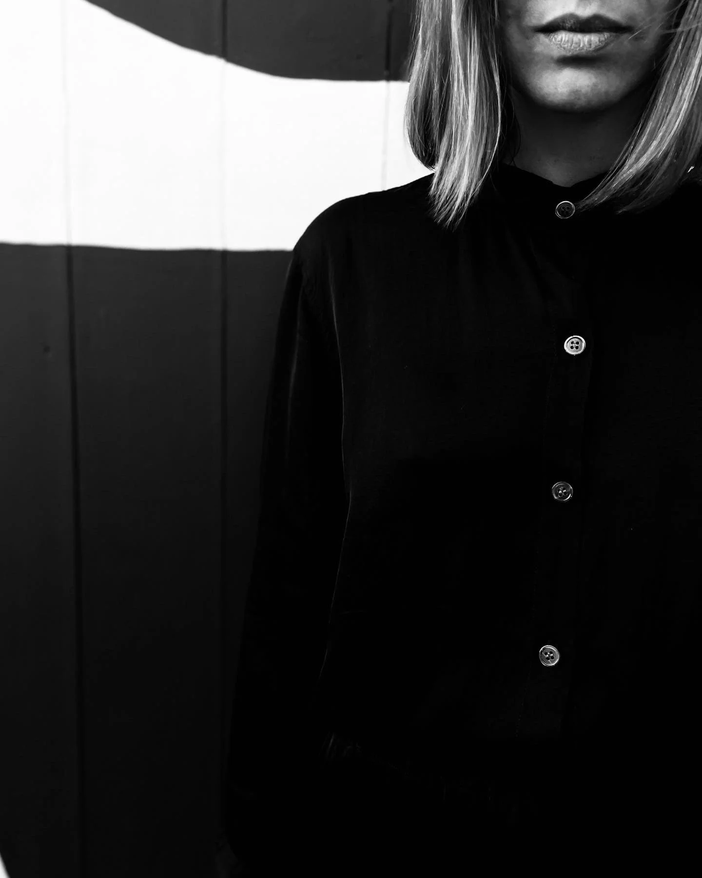 Close-up black and white photo of a woman's face and upper body, partially visible, with a background featuring horizontal stripes.