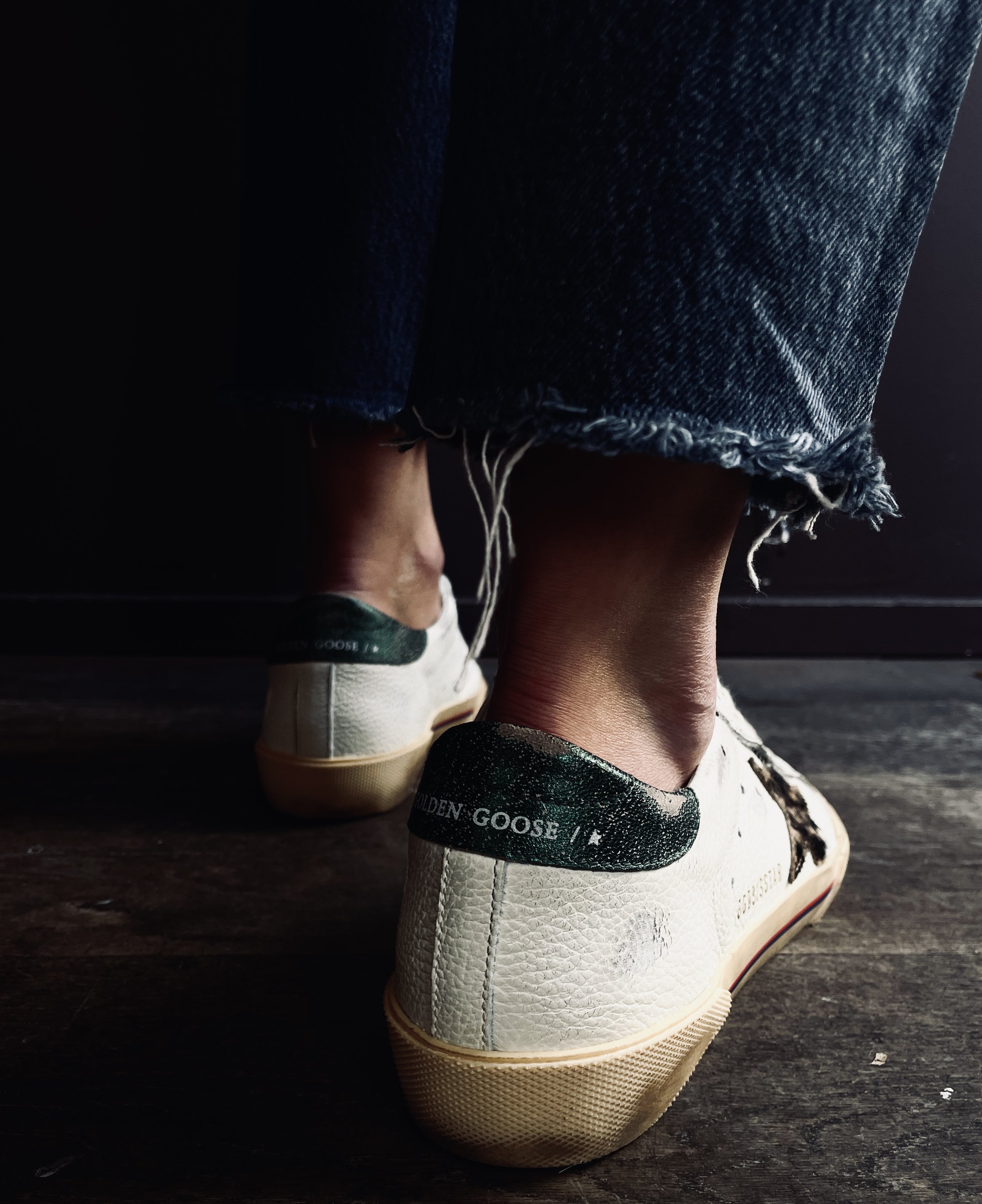 Close-up of a person's feet wearing white Golden Goose sneakers and frayed denim jeans.