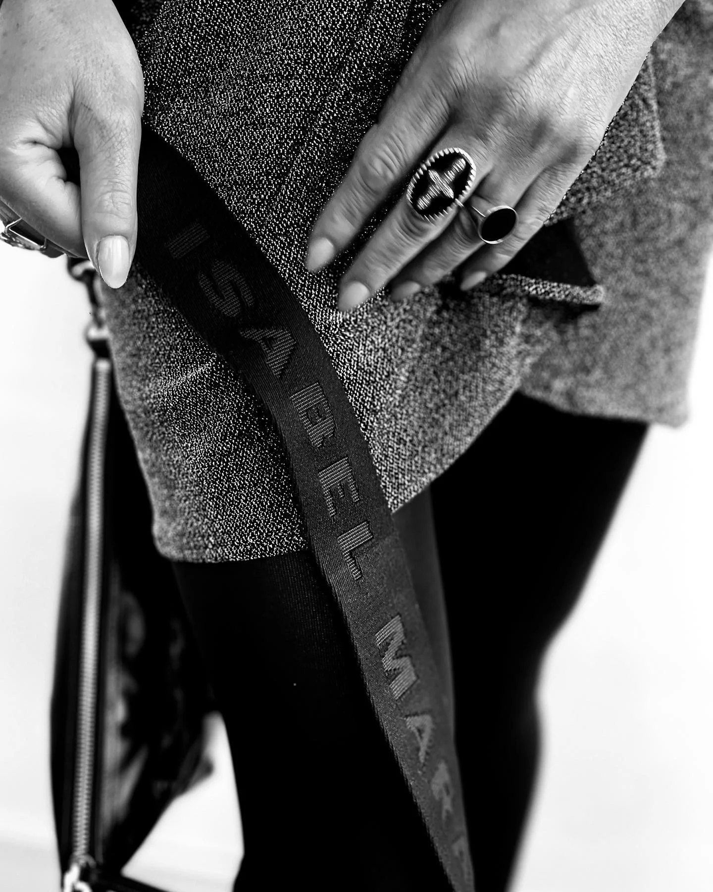 Close-up of a person's hand with rings, touching their textured sweatshirt highlighting the word 'SEE' on the sleeve, in black and white.