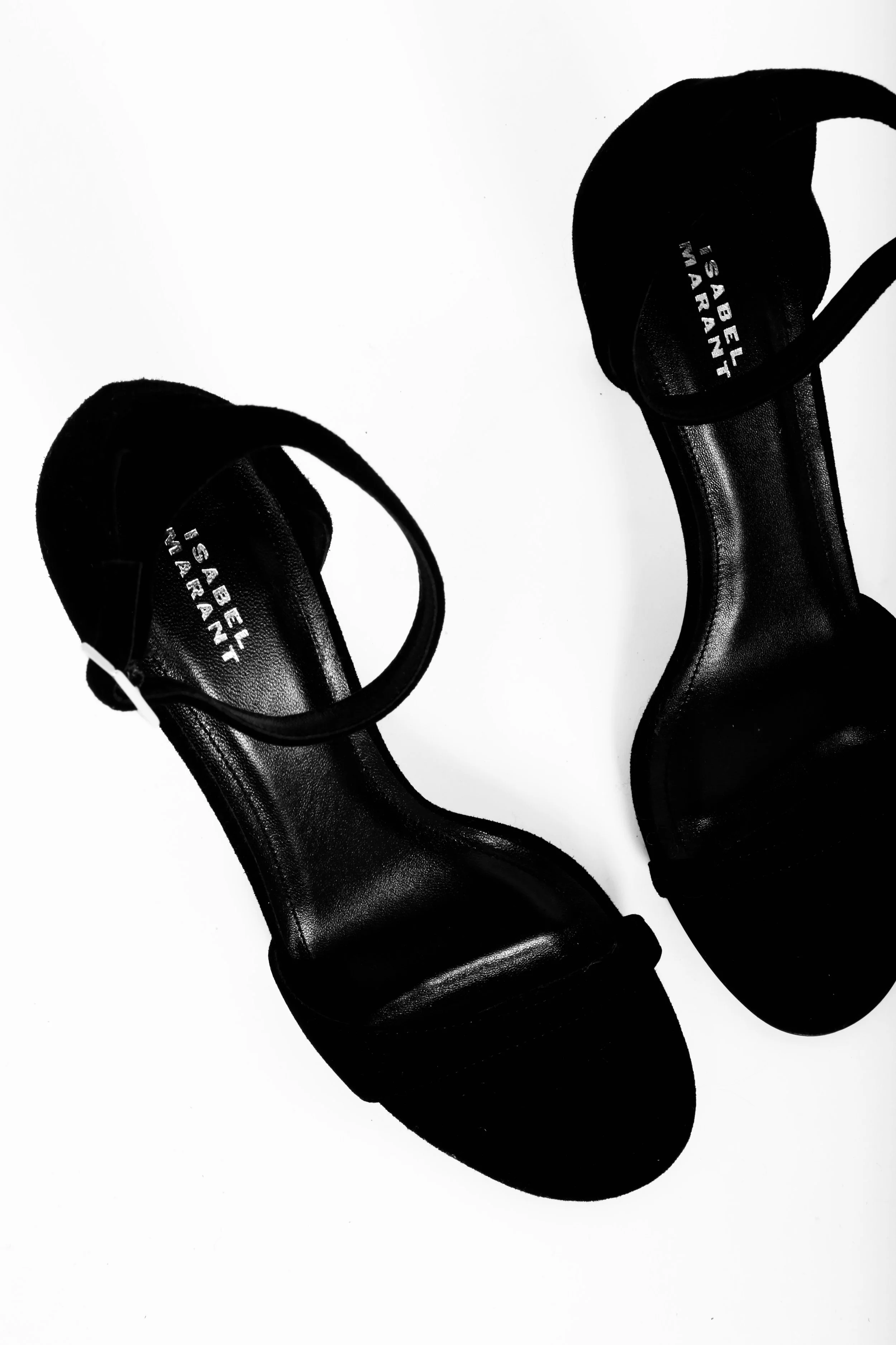 Black high-heeled sandals with ankle straps on a white surface.