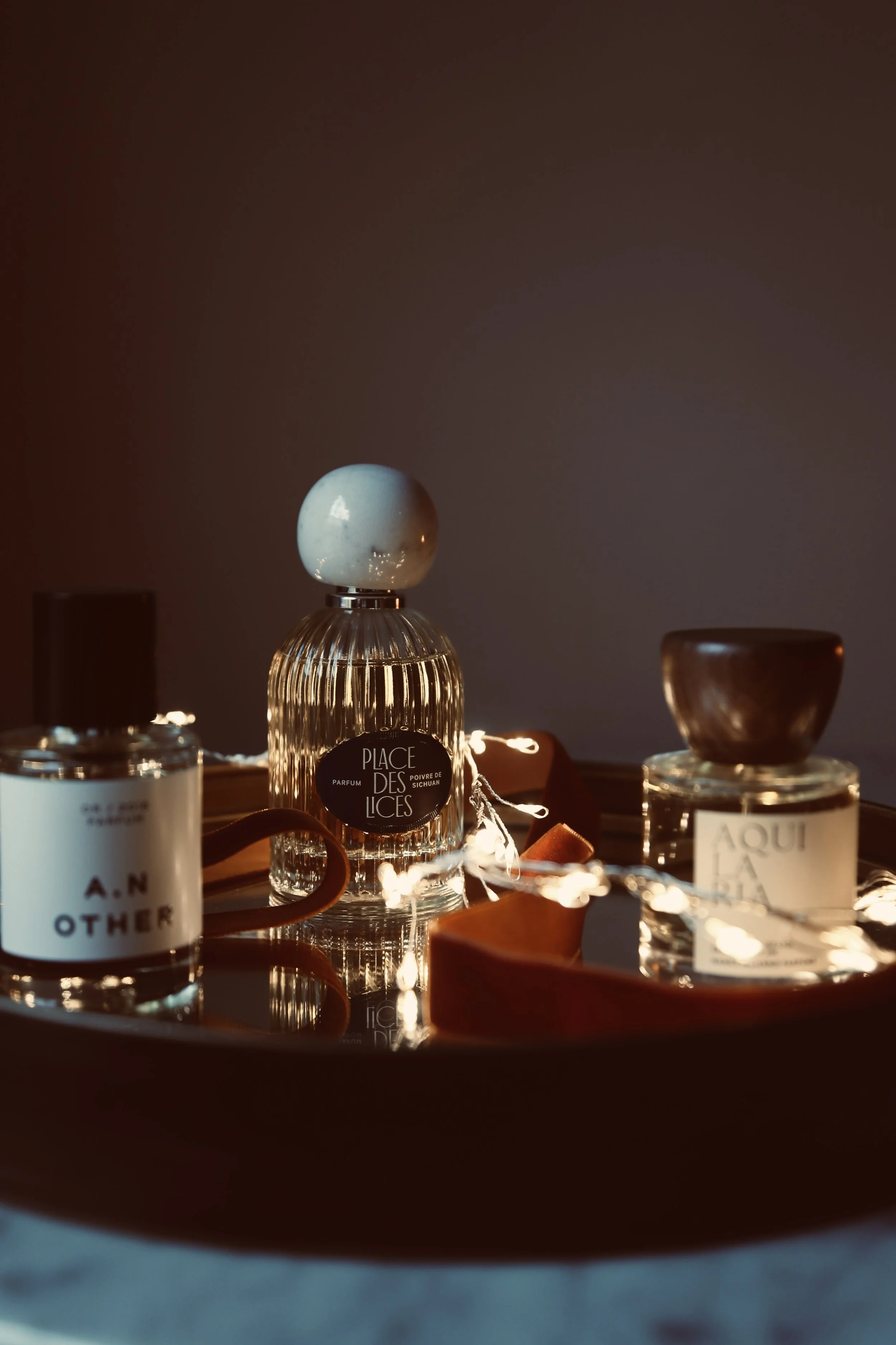 Decorative bottles of perfume on a reflective surface illuminated by string lights, with a dark background.