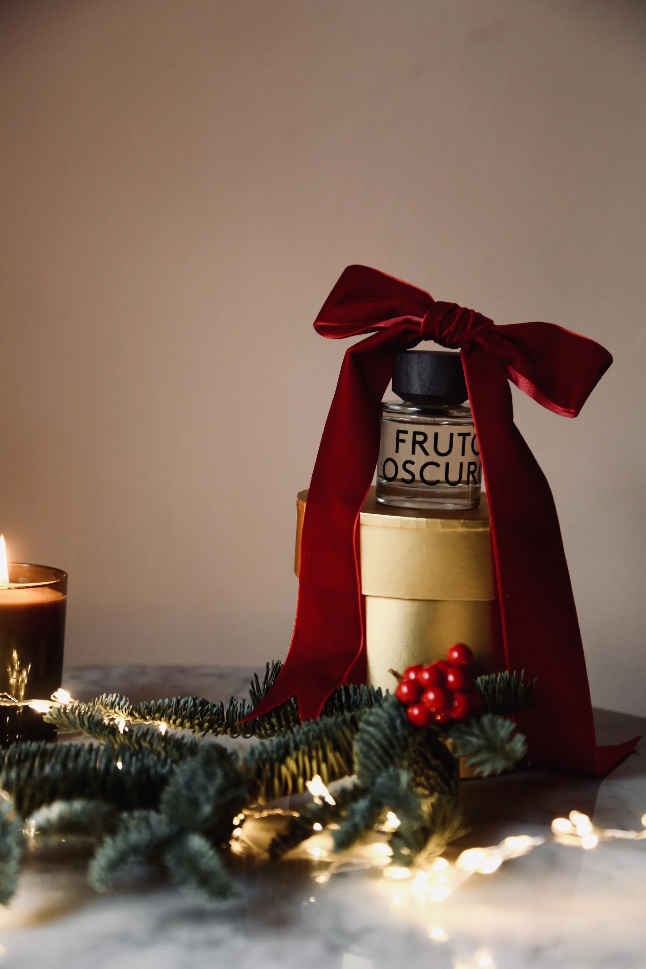 A holiday gift and candle on a table, decorated with pine branches and holiday lights.