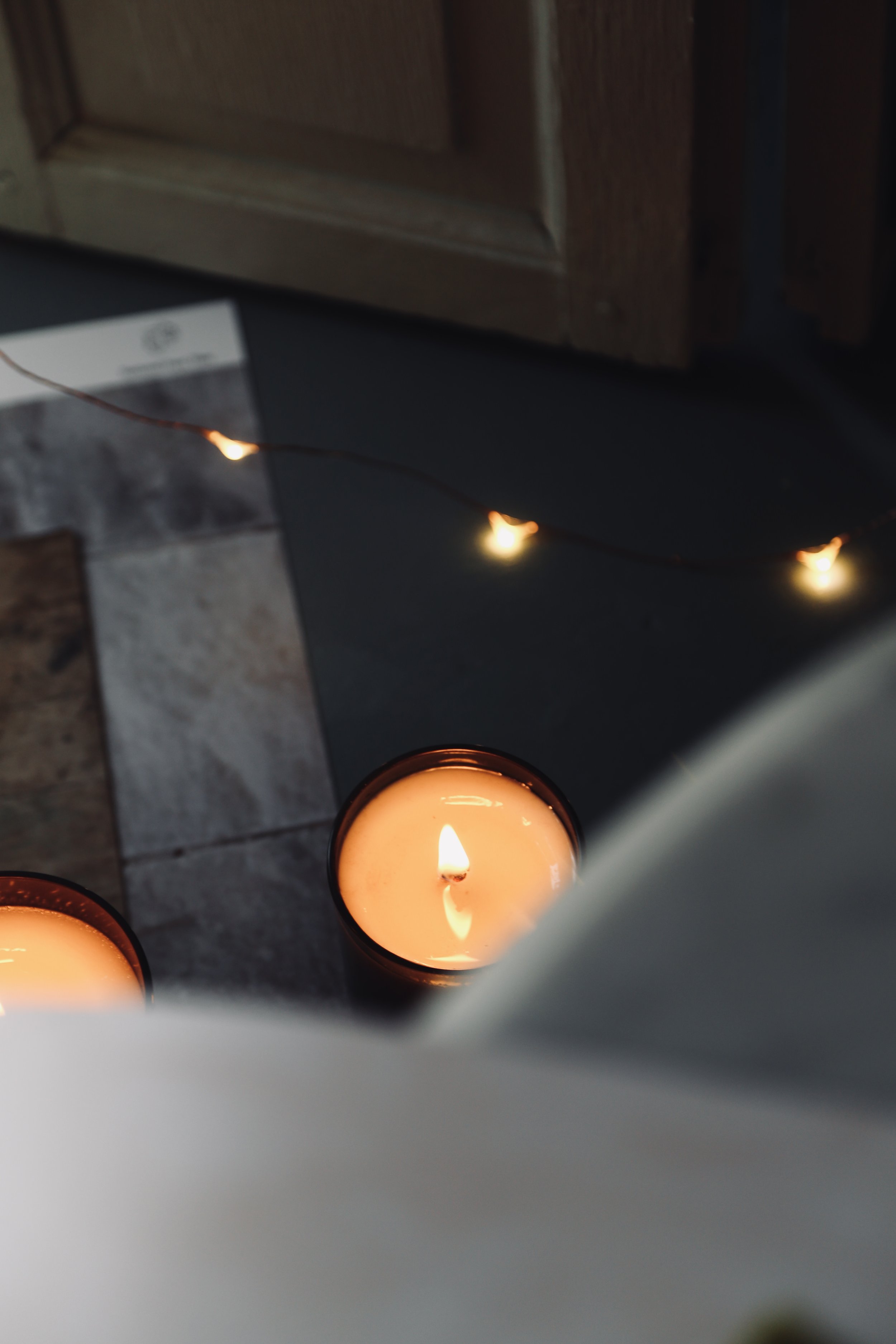 Several lit candles and a string of small warm-colored lights on a dark surface near wooden cabinets.