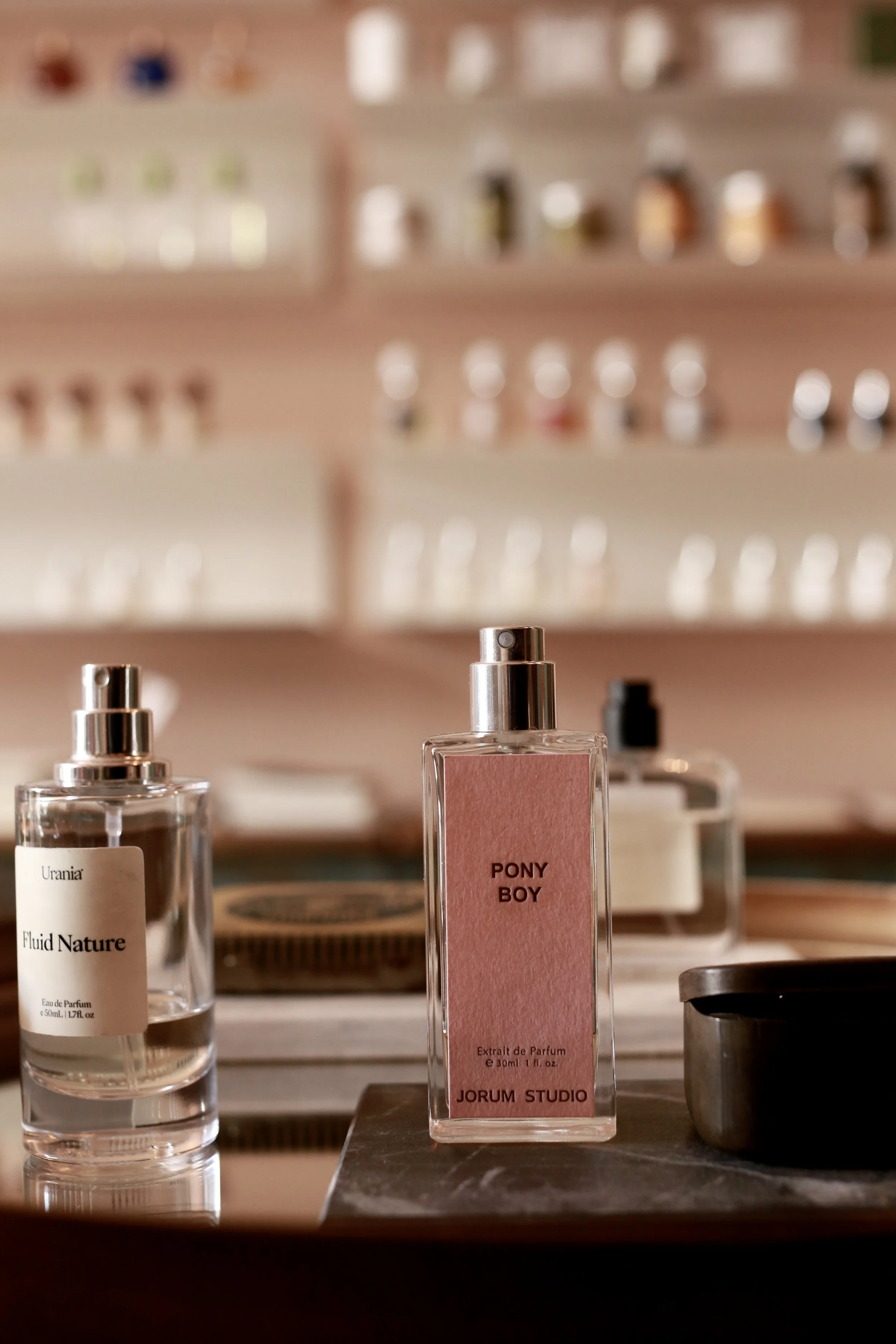 Close-up of bottles of perfume on a reflective surface with blurry shelves of beauty products in the background.