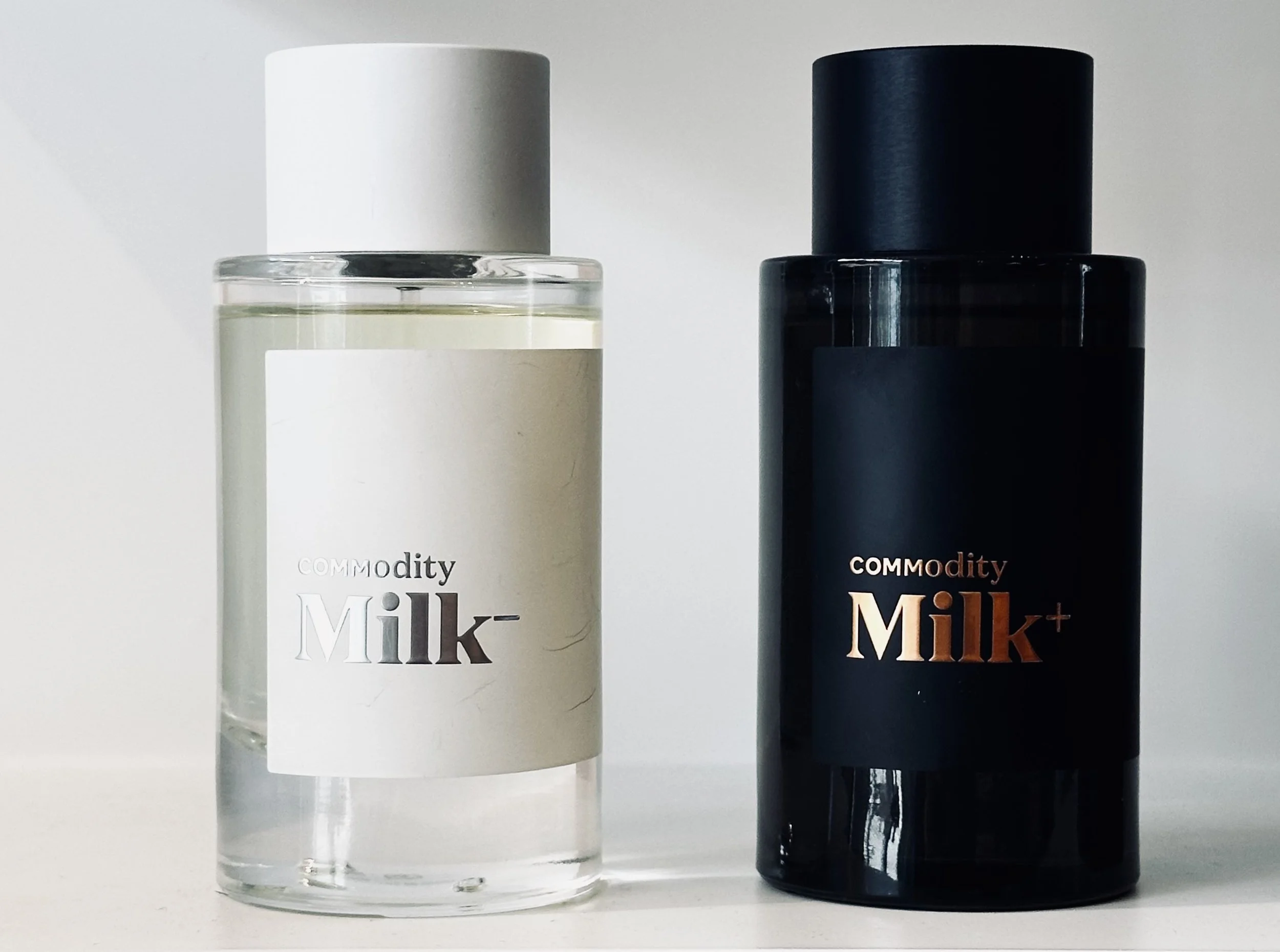 Two bottles of cosmetic products labeled 'Commodity Milk' and 'Commodity Milk+' on a white surface against a white background.