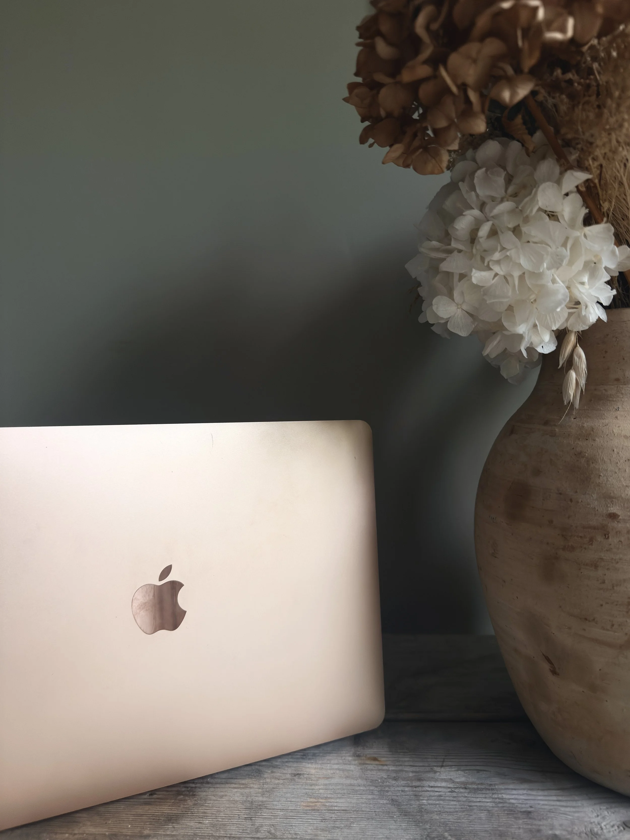 macbook laptop next to a beige vase with flowers