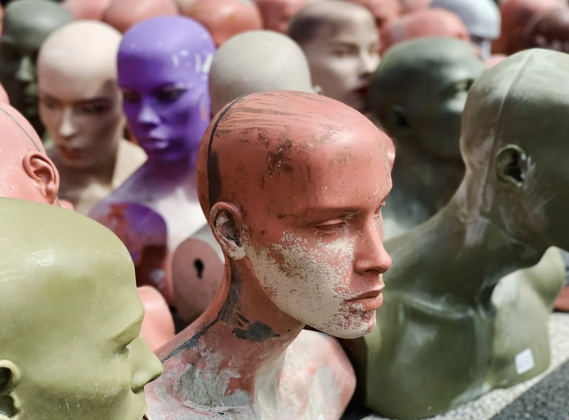 A collection of mannequin heads with various skin tones and colors, some with visible wear and scratches, arranged closely together.