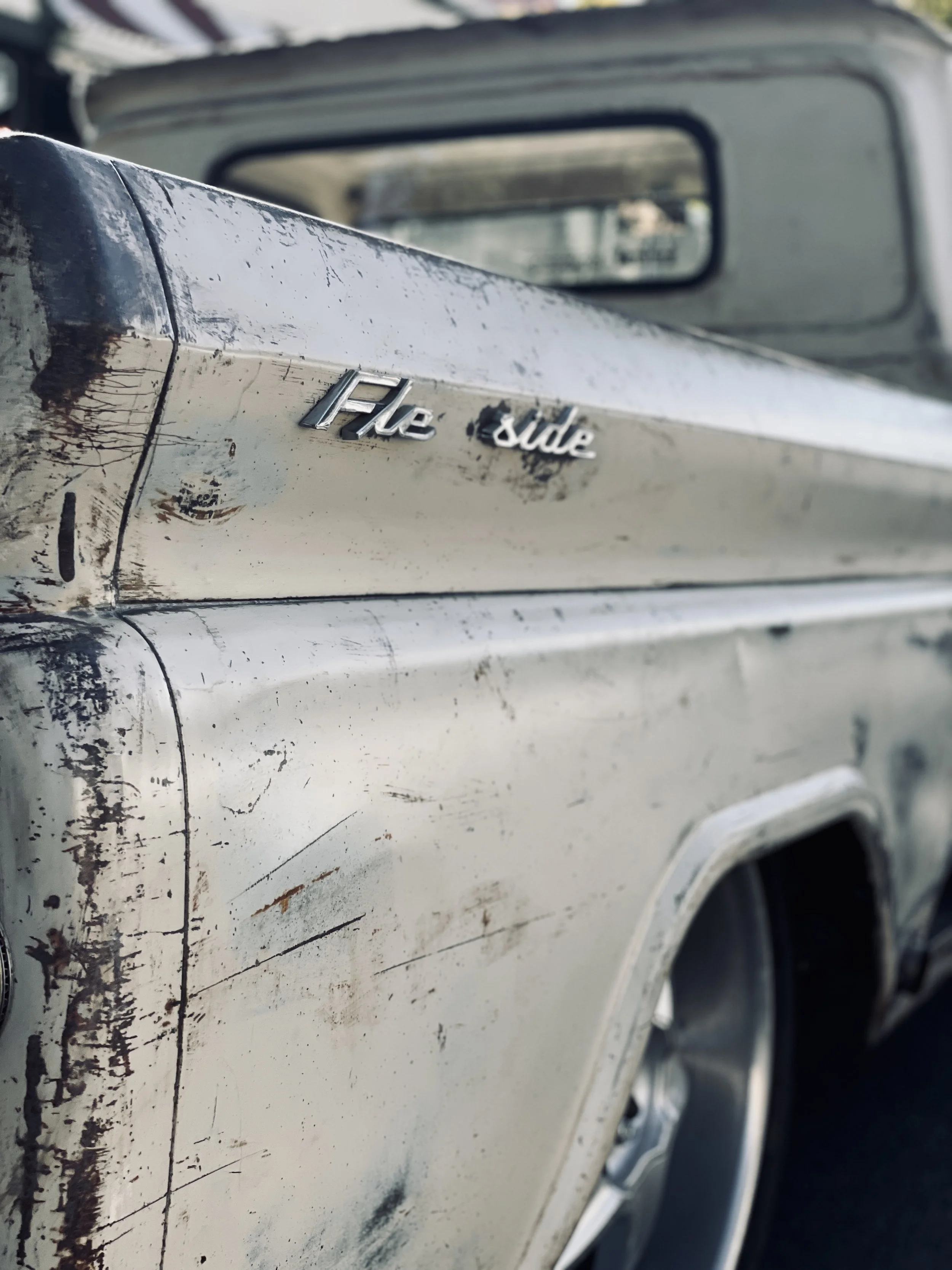 Close-up of a vintage pickup truck with a white, weathered, and scratched exterior, showing the chrome 'Fle Sure' badge on the side.