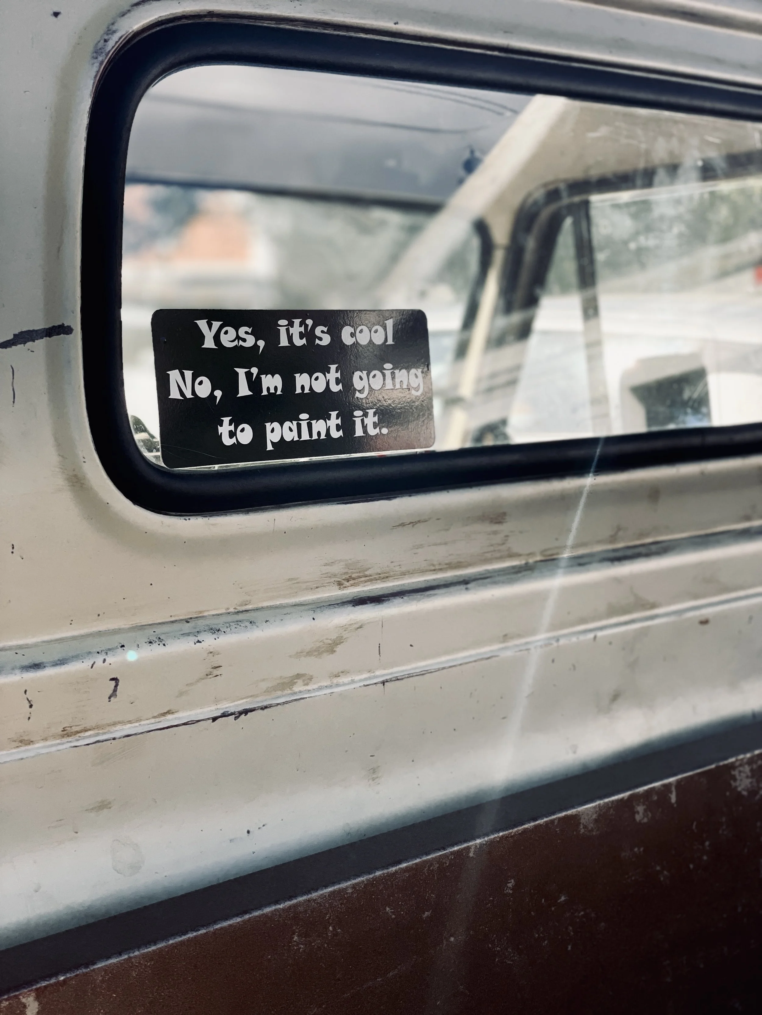 A rectangular black sticker with white text on a vehicle window. The sticker says, 'Yes, it's cool. No, I'm not going to paint it.'