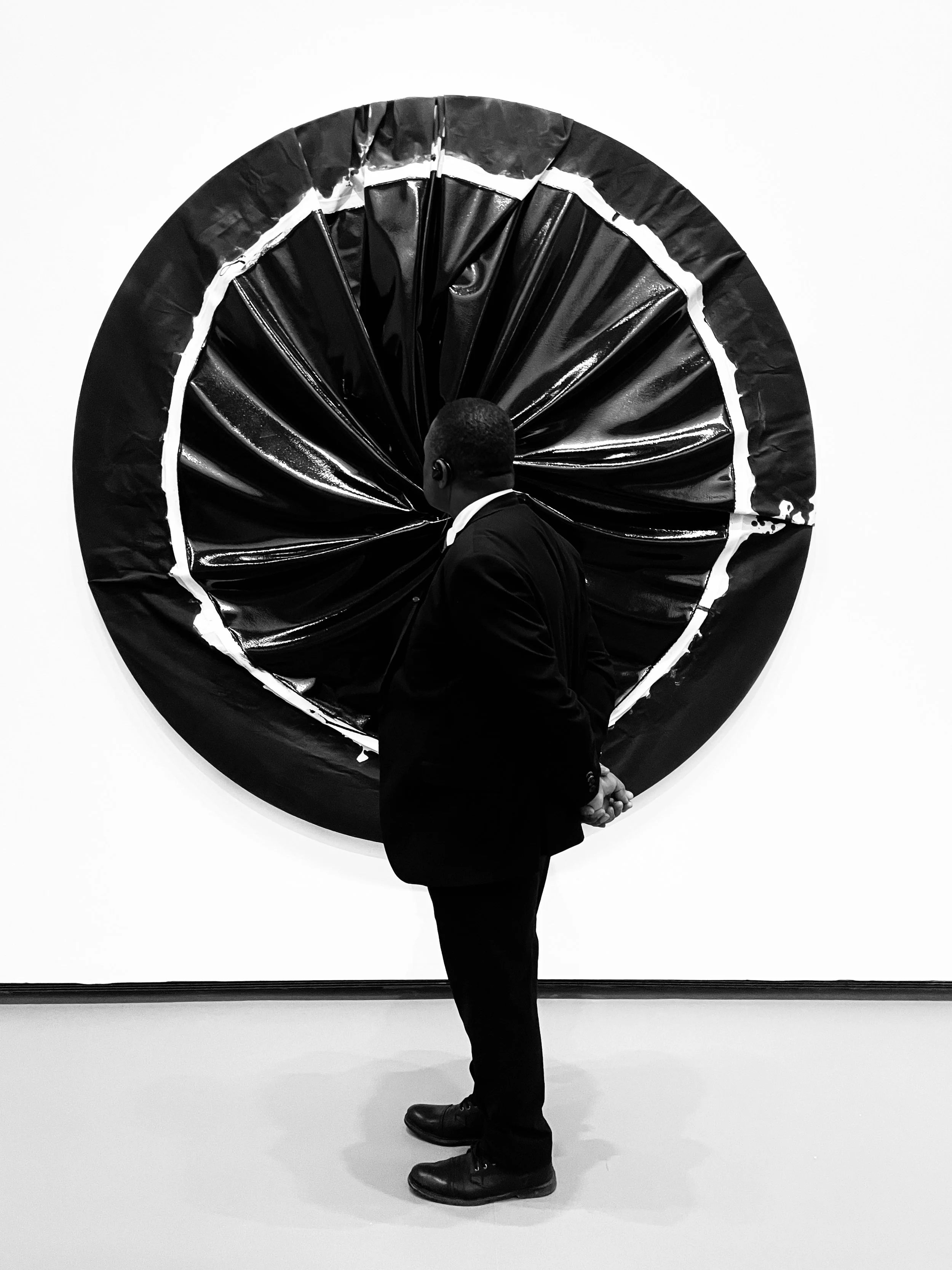A man in a suit observing an abstract black and white textured circular artwork on a gallery wall.