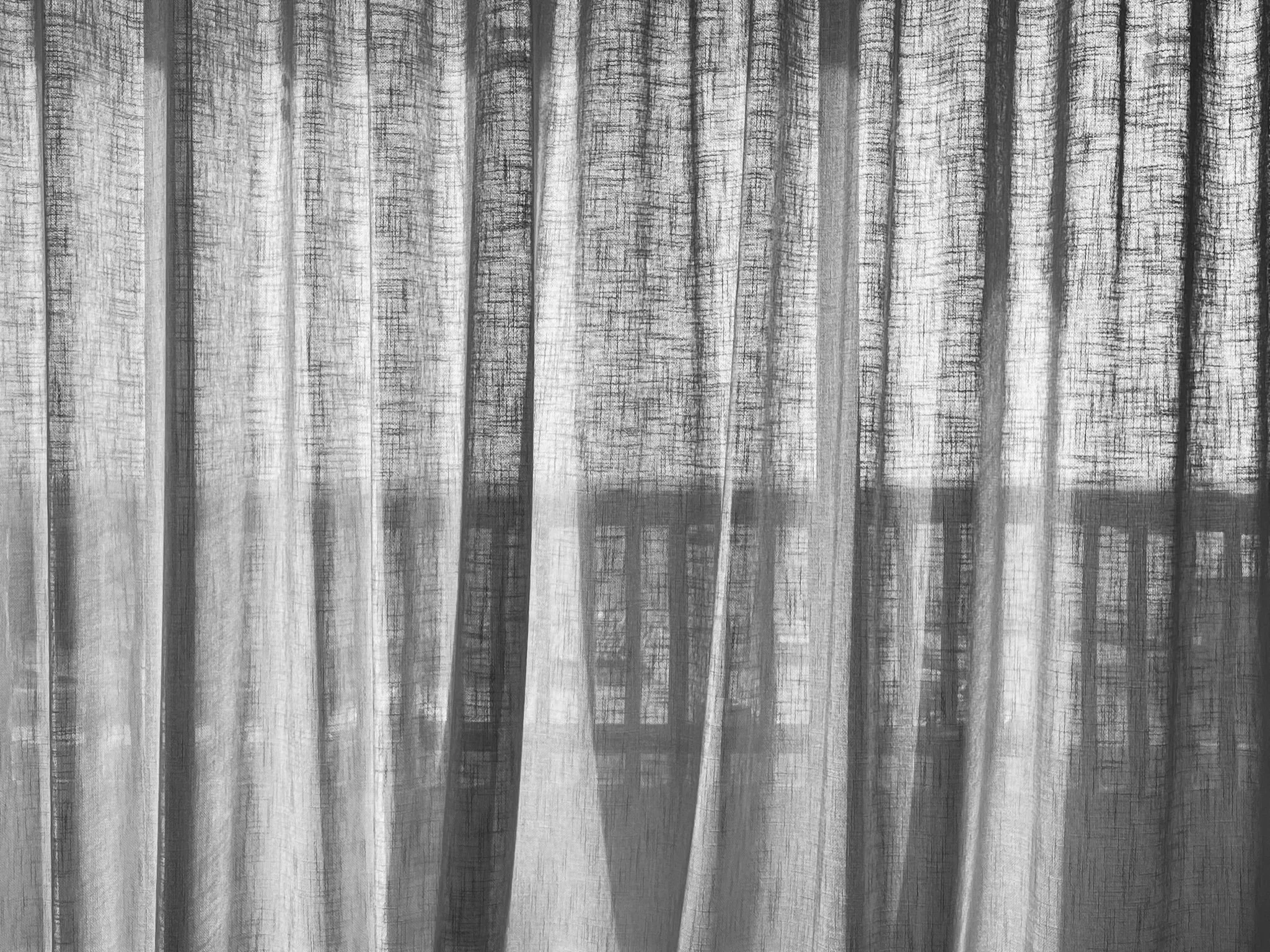 View through a sheer curtain showing a building with multiple windowpanes in the background.