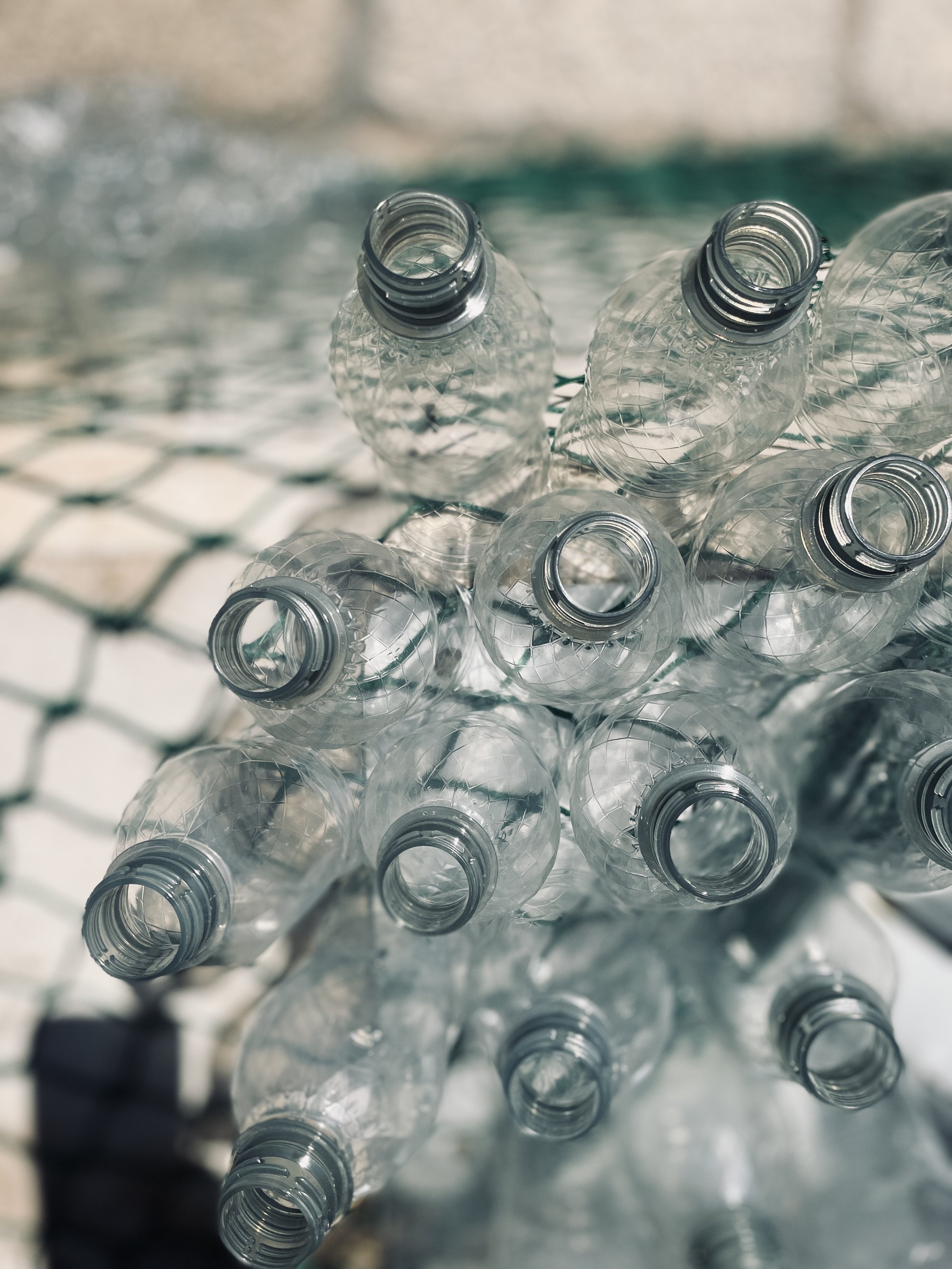 A cluster of empty transparent plastic bottles with open tops, placed on a wire mesh surface.
