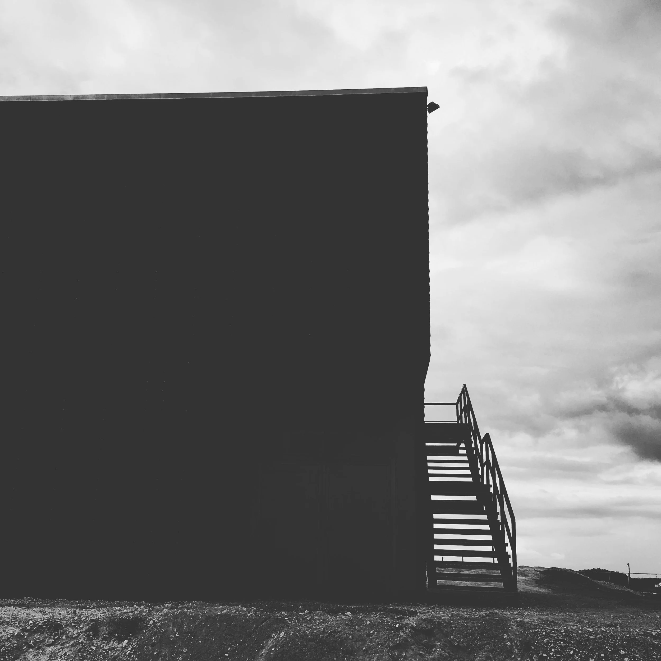 Silhouette of a building with an external staircase against a cloudy sky.