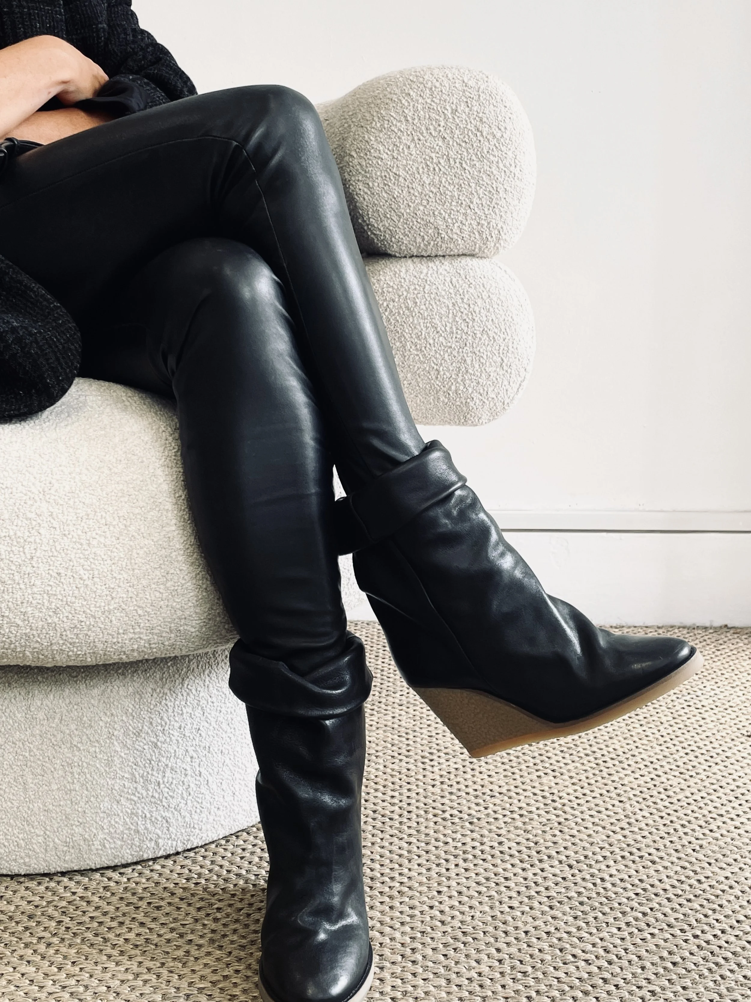 Person sitting on a white textured sofa wearing black leather over-the-knee boots and black leather pants.