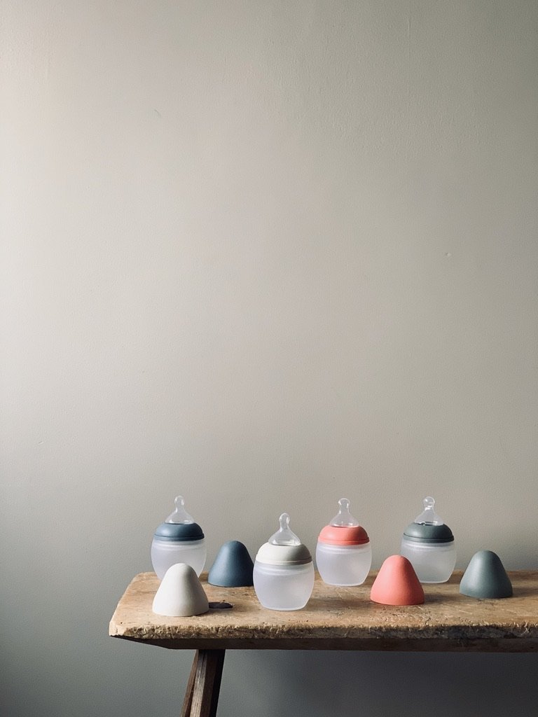 A wooden table with baby bottles and colorful pacifiers arranged on it against a plain light gray wall.