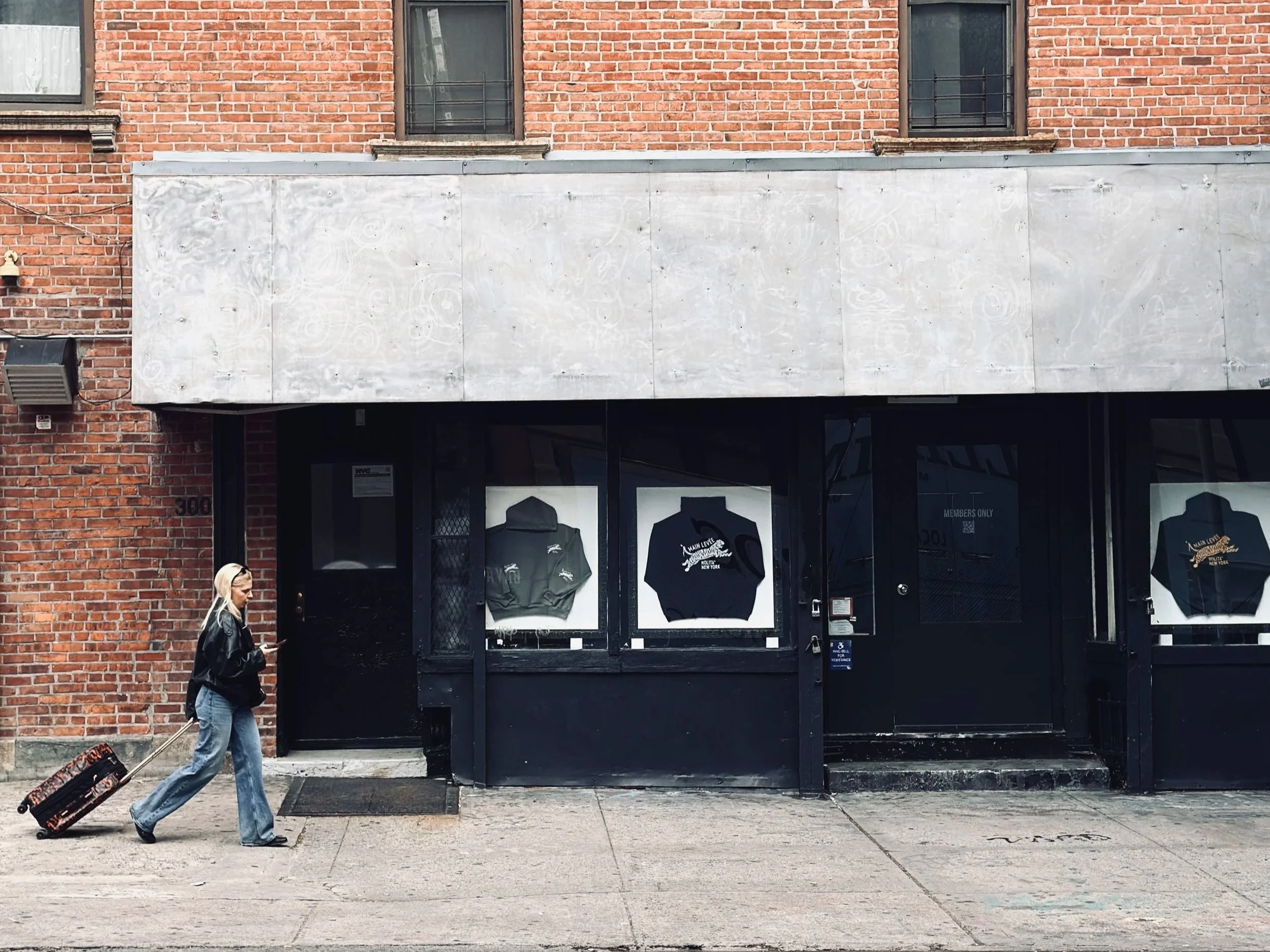 Black storefront with branded hoodies in the windows, traveller with a suitcase walking past, New York