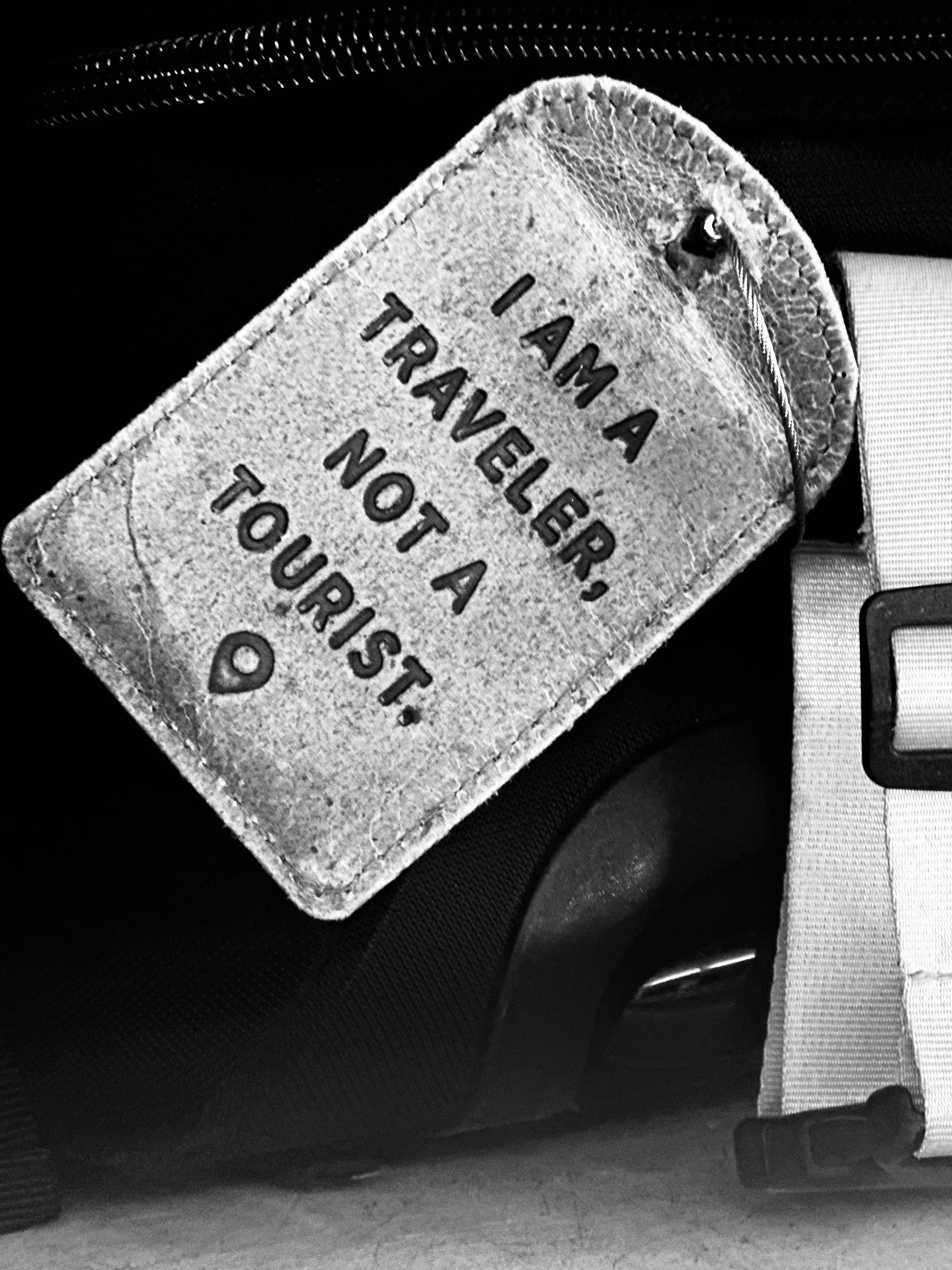 A luggage tag with the text 'I AM A TRAVELER, NOT A TOURIST.' attached to a piece of luggage.