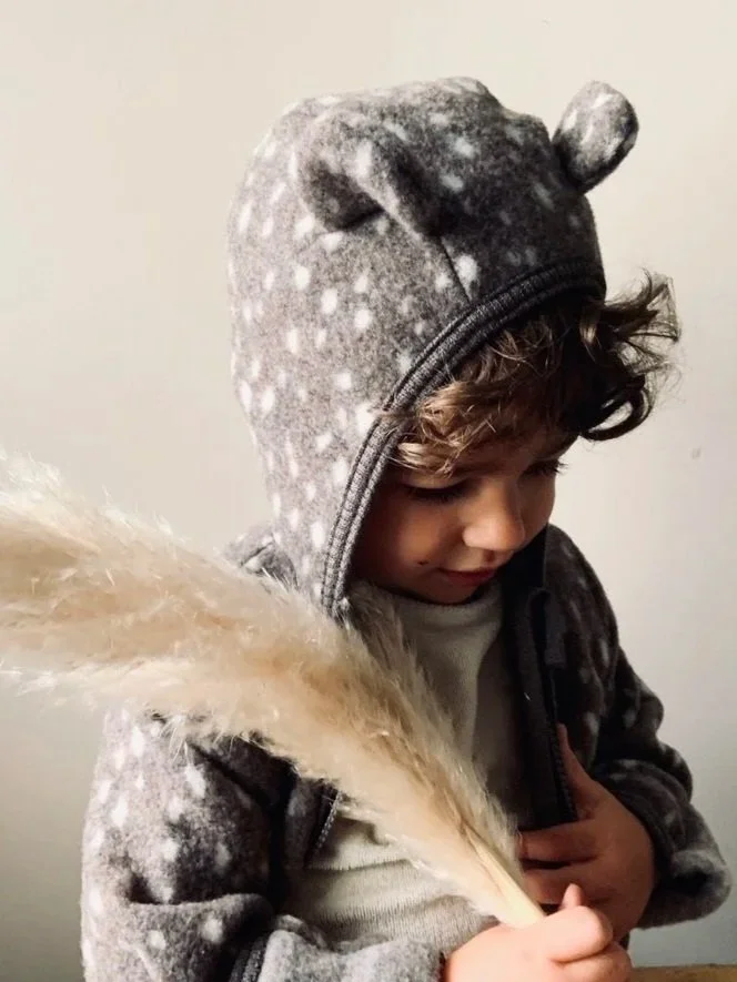 Child wearing a bear hoodie holding a large feather.