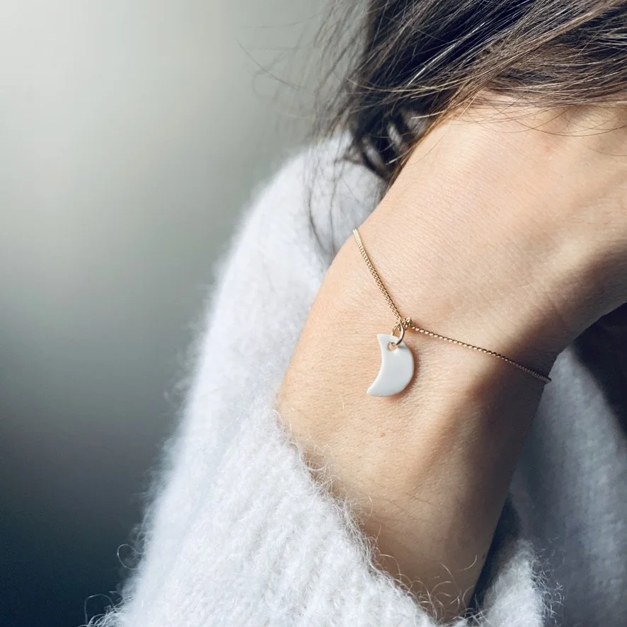 A woman wearing a delicate gold chain necklace with a moon-shaped white pendant.