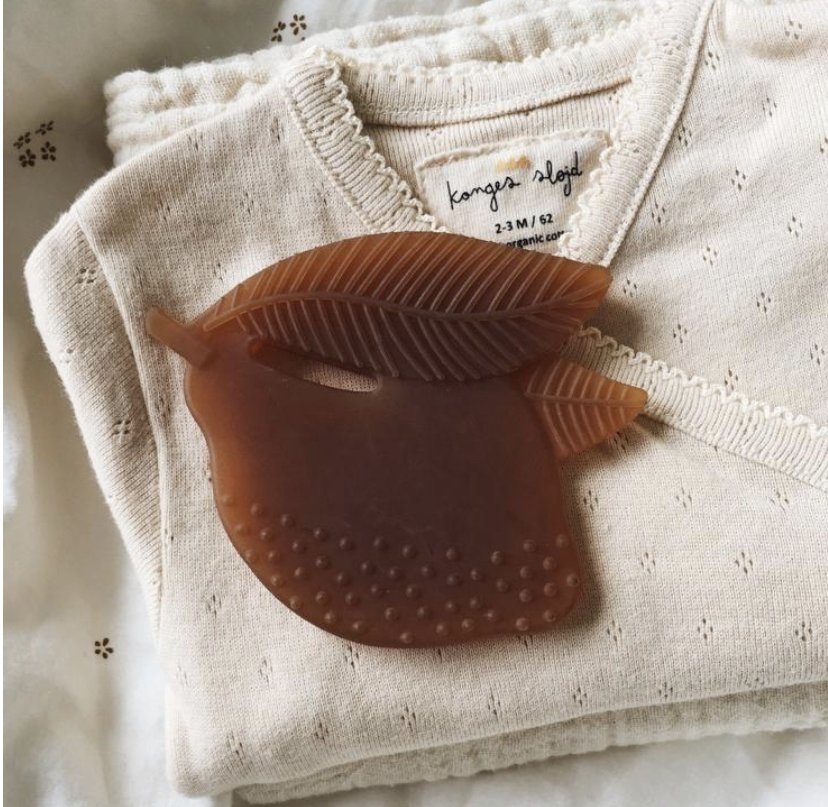 A brown apple-shaped brooch with leaf details, placed on a folded white knit shirt.