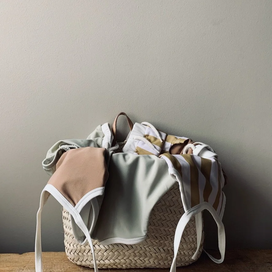 A laundry basket filled with various clothing items, including bras and underwear, placed on a wooden surface against a plain wall.