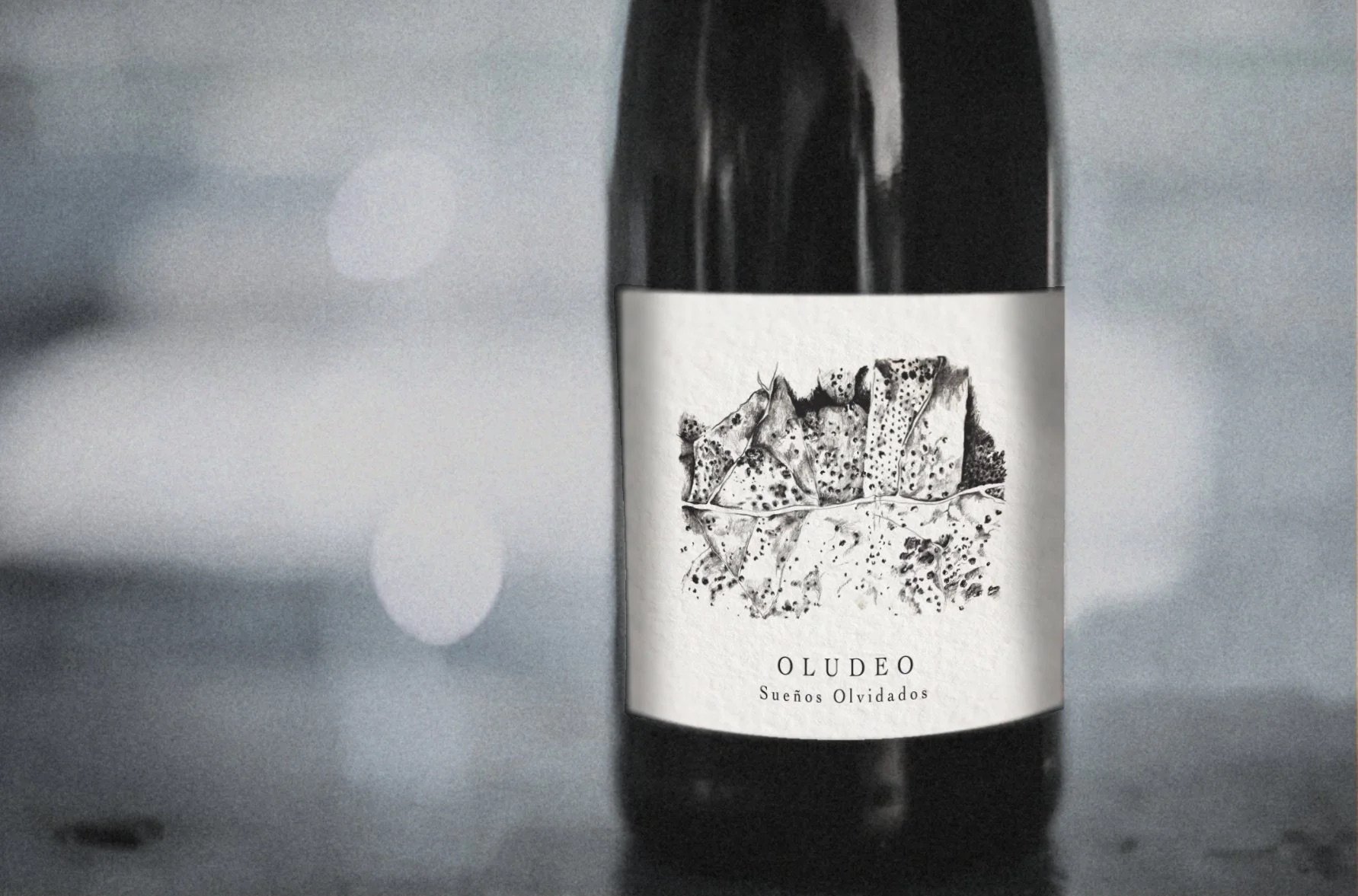 A black wine bottle with a white label featuring an abstract black and white illustration and the text 'OLUDEO Sueños Olvidados.'