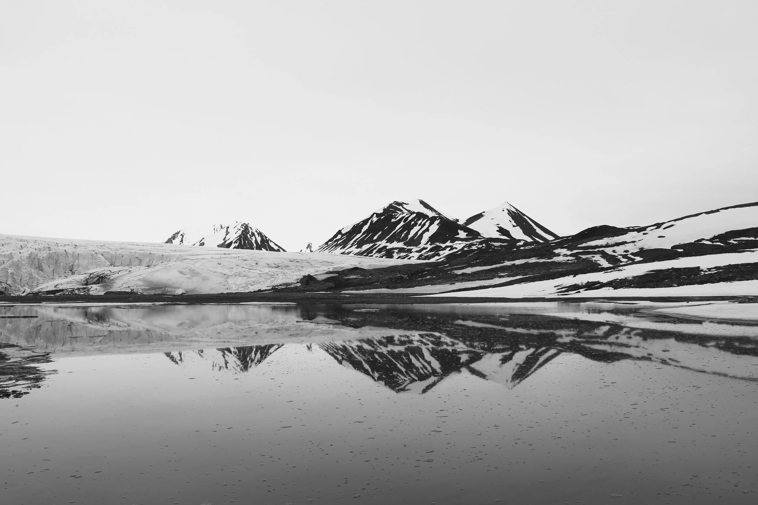 Black and white photograph of snow-capped mountains reflected in a calm lake.