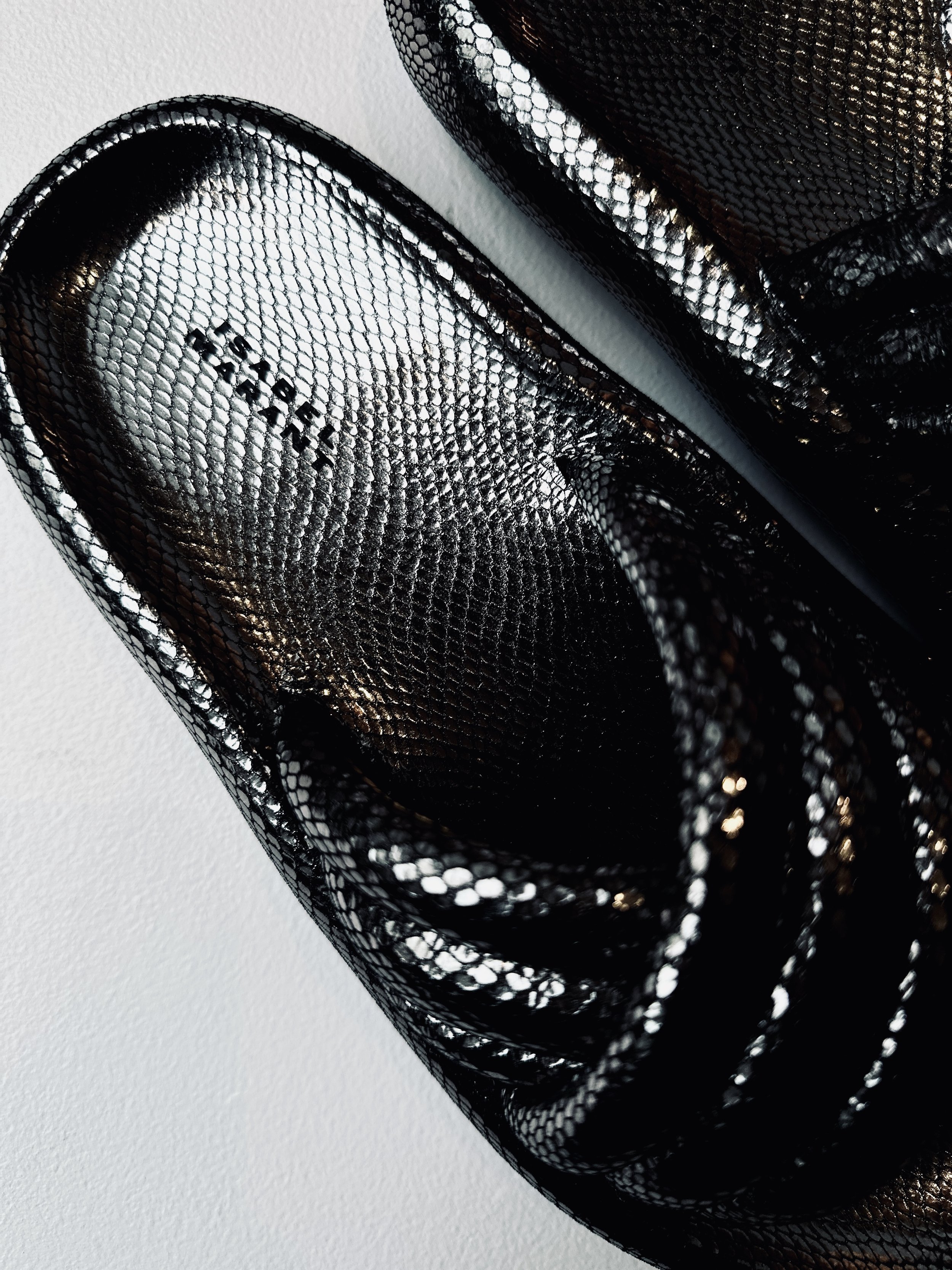 Close-up of a pair of black mesh high-heeled shoes with a shiny, textured surface, photographed against a light background.