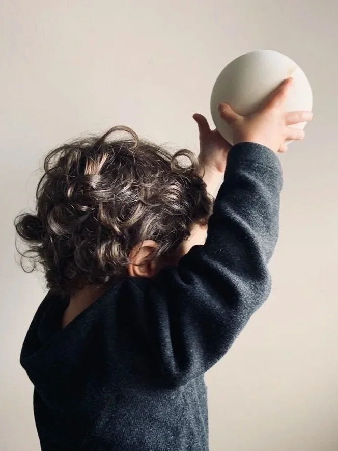 A young child with curly hair holding a spherical object above their head.