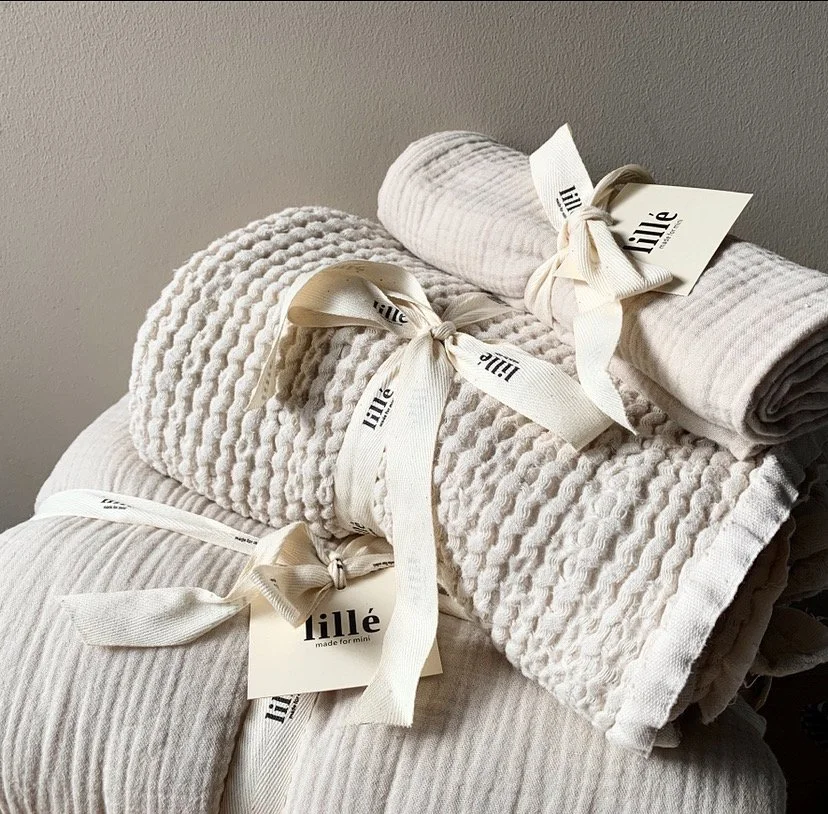 Knitted baby shoes tied with ribbon styled on neutral surface, lifestyle product photography by MUSE Creative Studio Brighton
