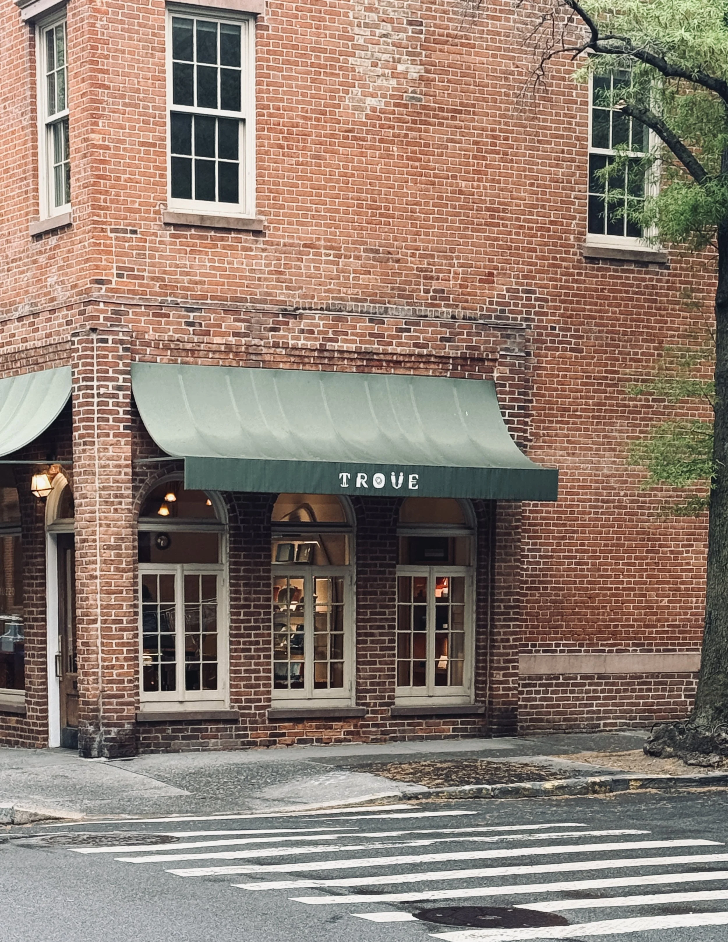 Red-brick corner building with a green Trove awning and arched windows, New York