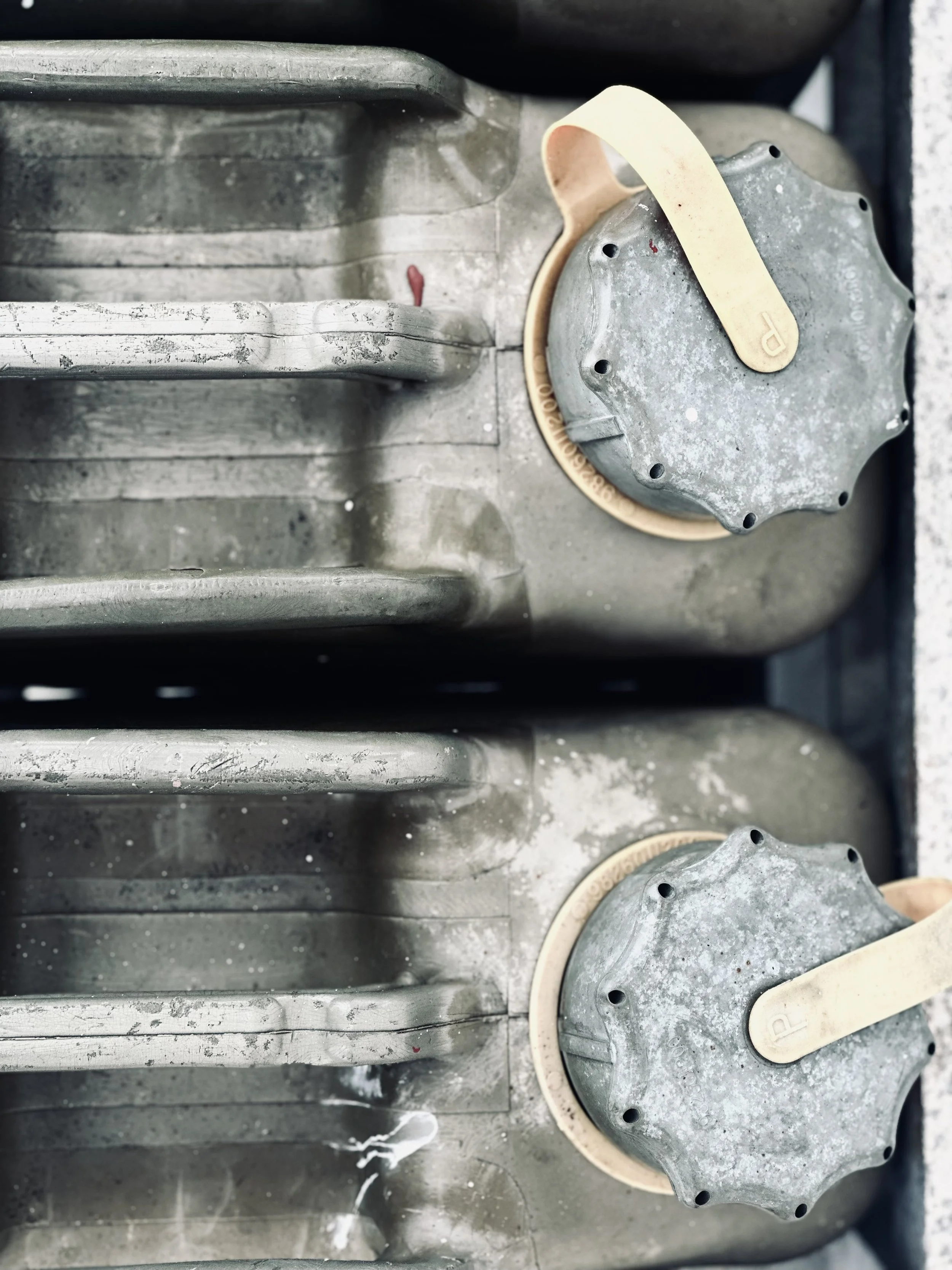 Two metal fuel containers with attached beige-colored caps and handles, showing signs of wear and dirt.