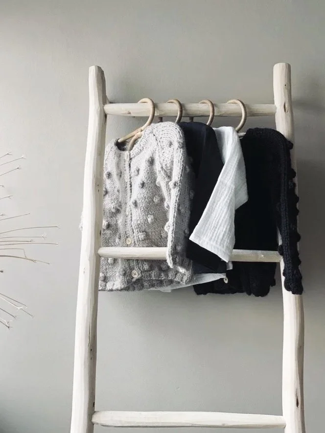 White wooden ladder rail hung with children's clothes in white, black and grey