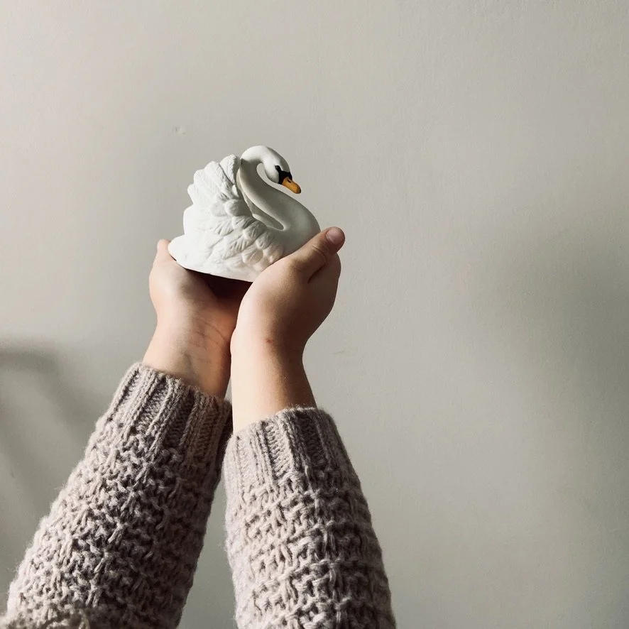 Two hands holding a small ceramic swan figure against a plain white background
