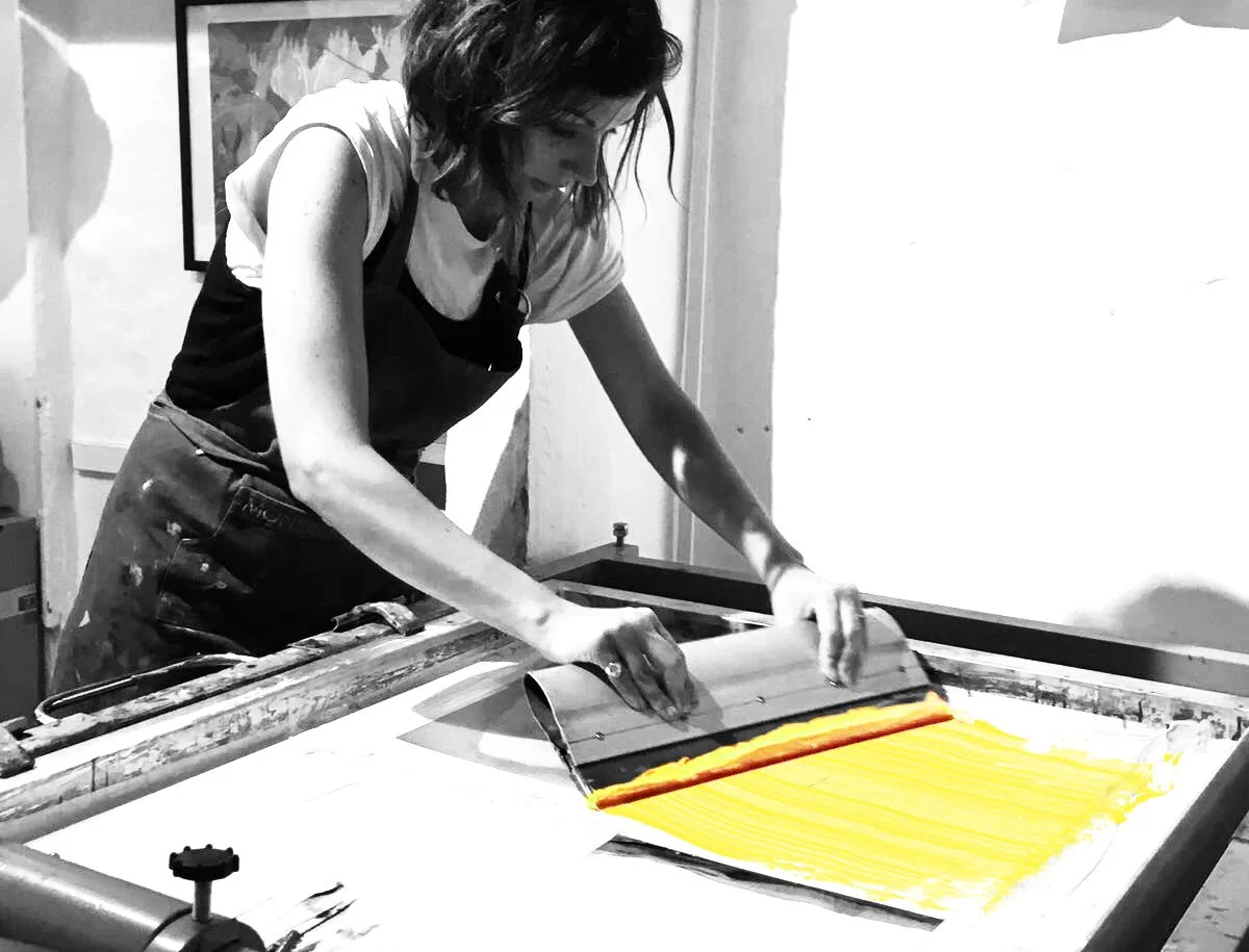 A person is using a printing press to create a yellow woodblock print, with the text being transferred onto paper.