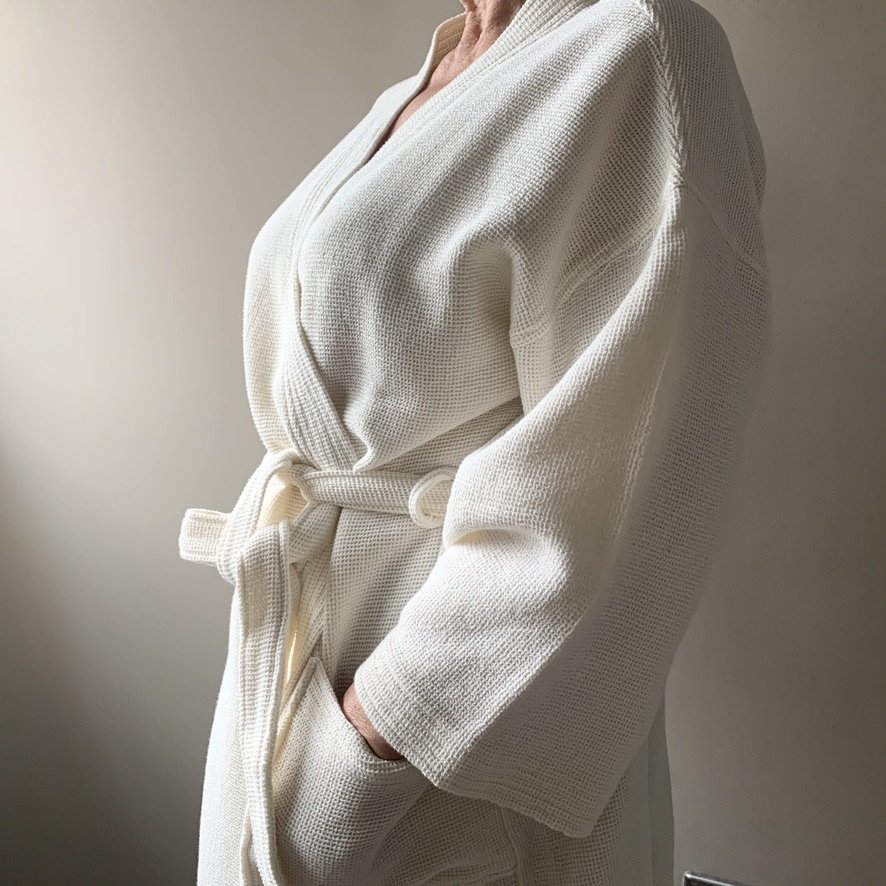 Close-up of a person wearing a cream-colored waffle-knit robe with a belt, standing against a plain light background.