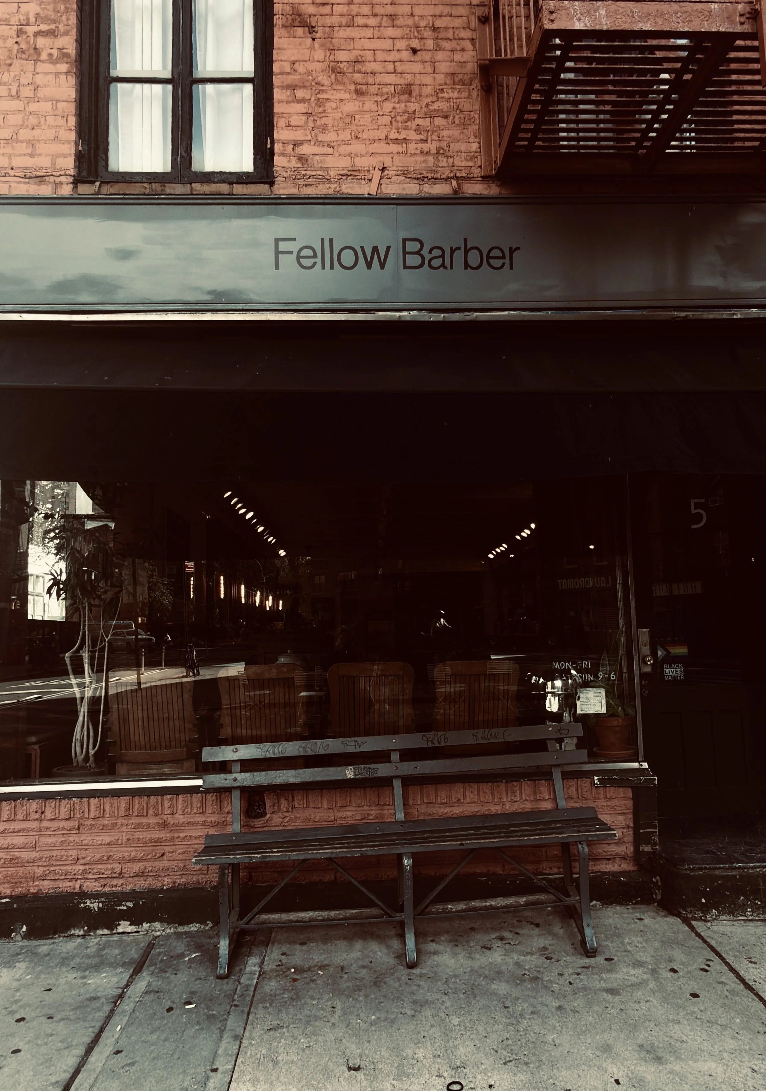 ellow Barber storefront with black signage and a wooden bench outside, New York