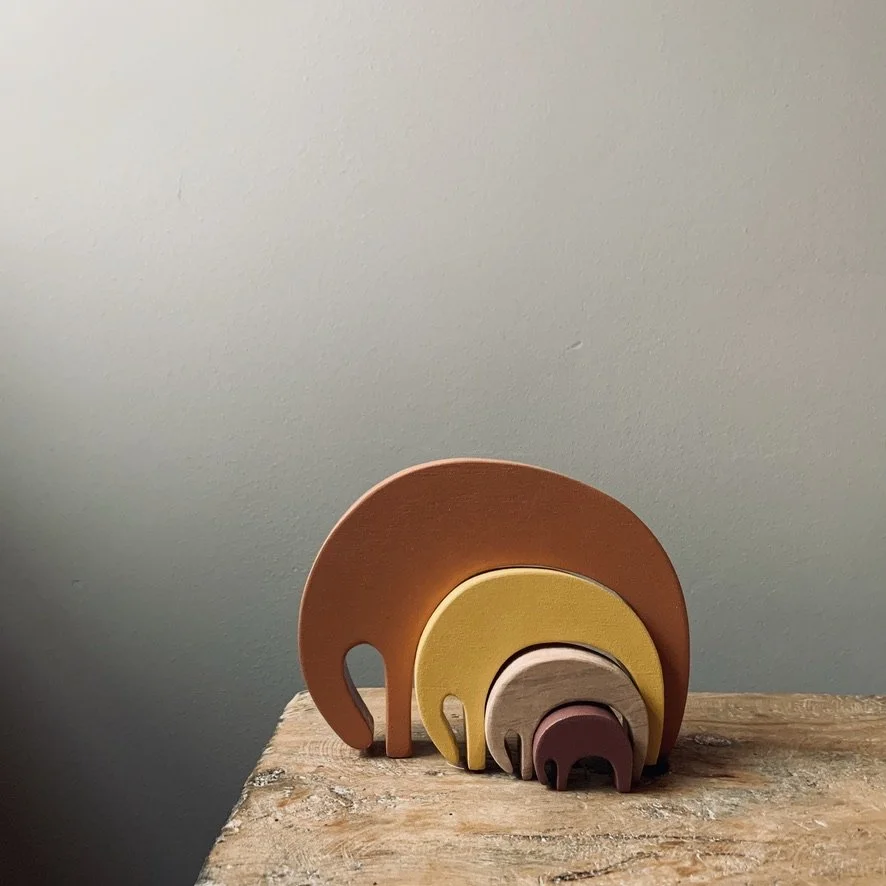 Set of four nested wooden elephant figures in orange, yellow, beige, and burgundy, arranged on a rustic wooden surface.