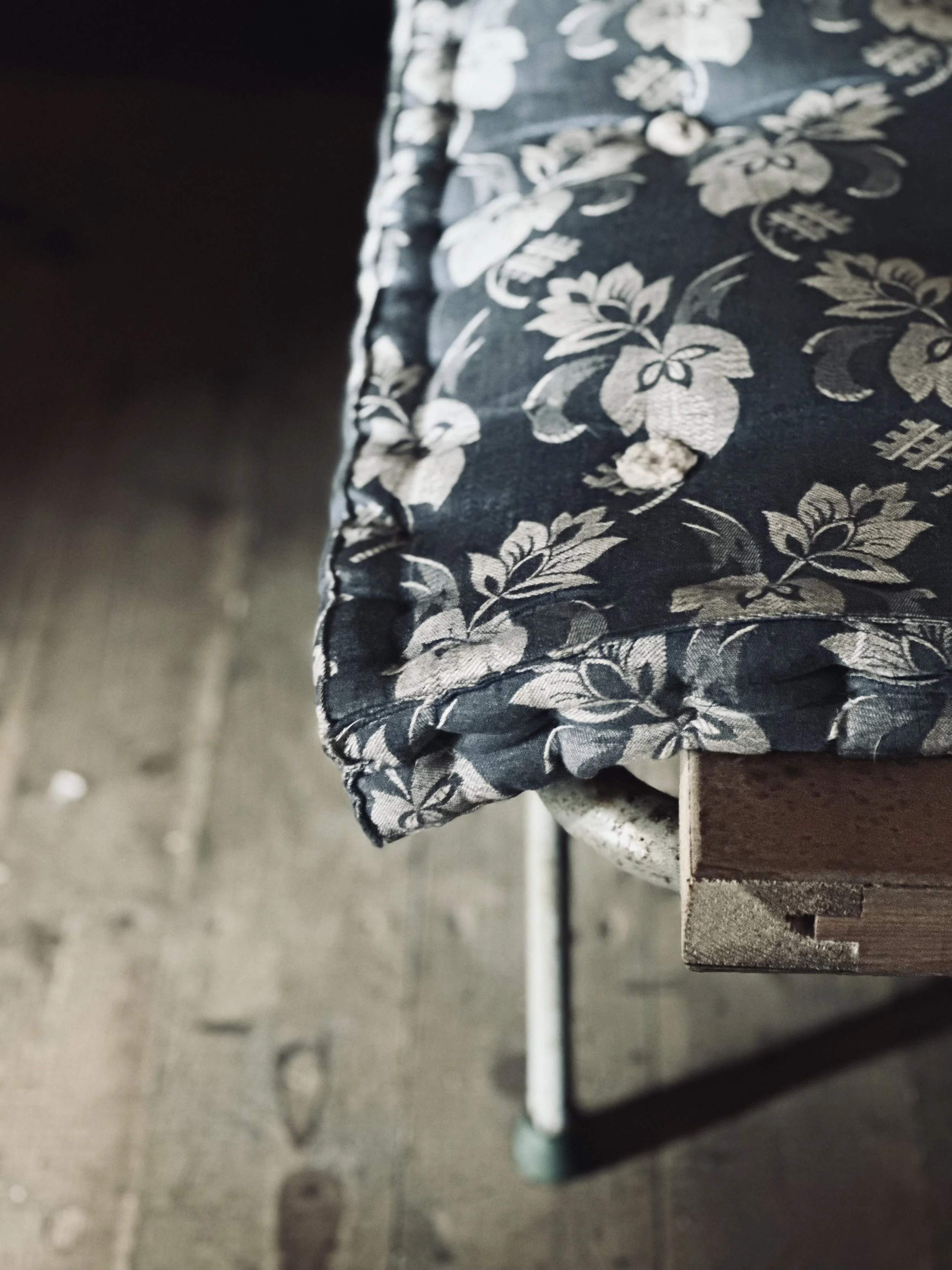 Close-up of a fabric with a floral pattern draped over the edge of a wooden table with metal legs, on a wooden floor.
