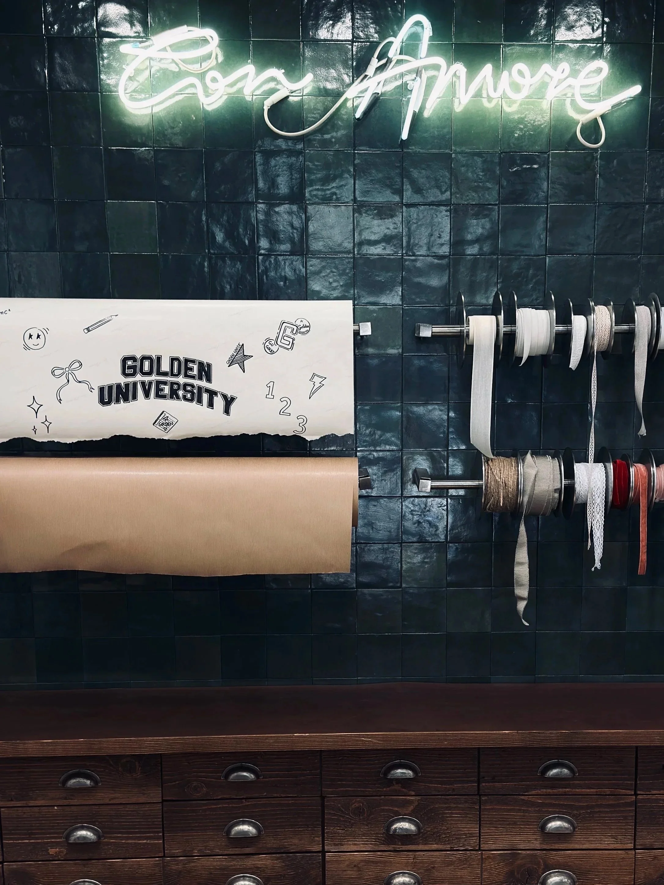 Con Amore neon script over dark green tiles, ribbon spools and Golden University card, New York shop interior