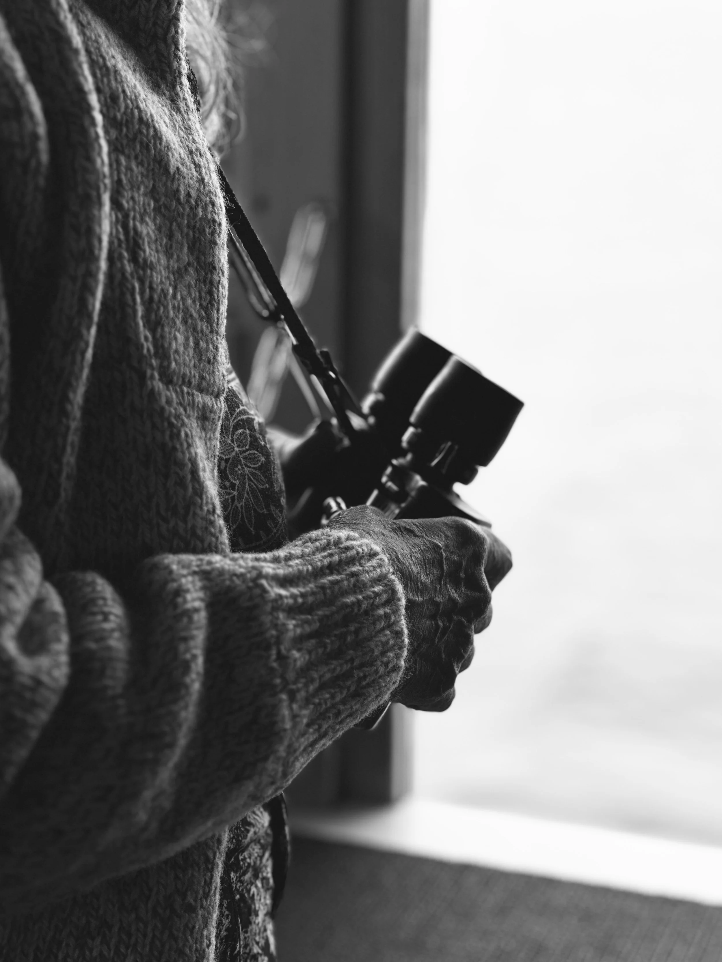 Person holding a telescope indoors near a window.