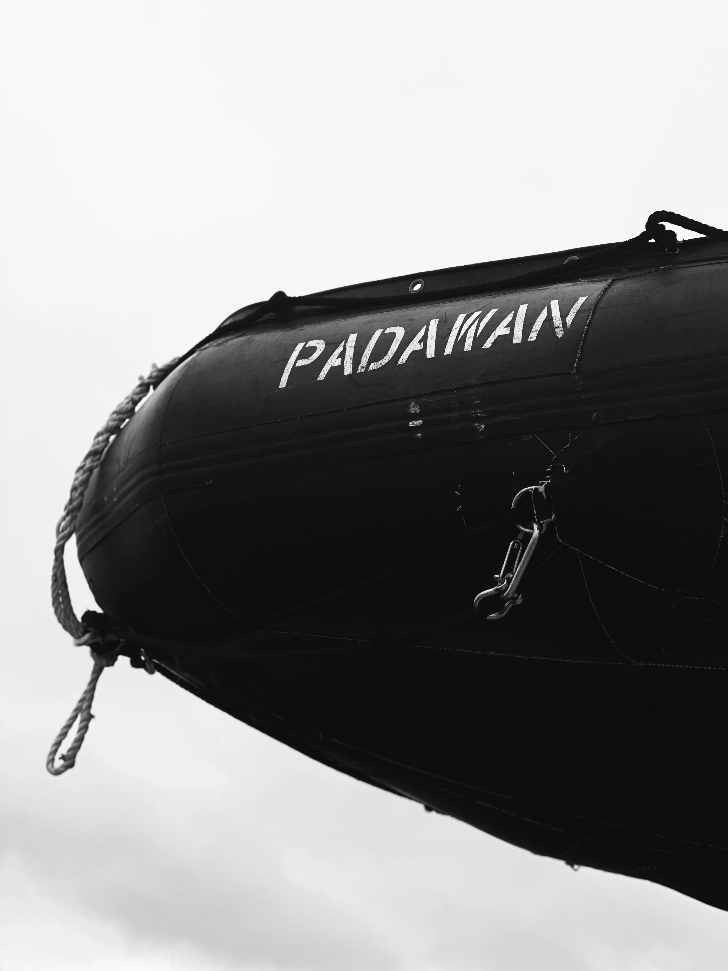 Black inflatable boat with the word PADAWAN written on it, against a cloudy sky.