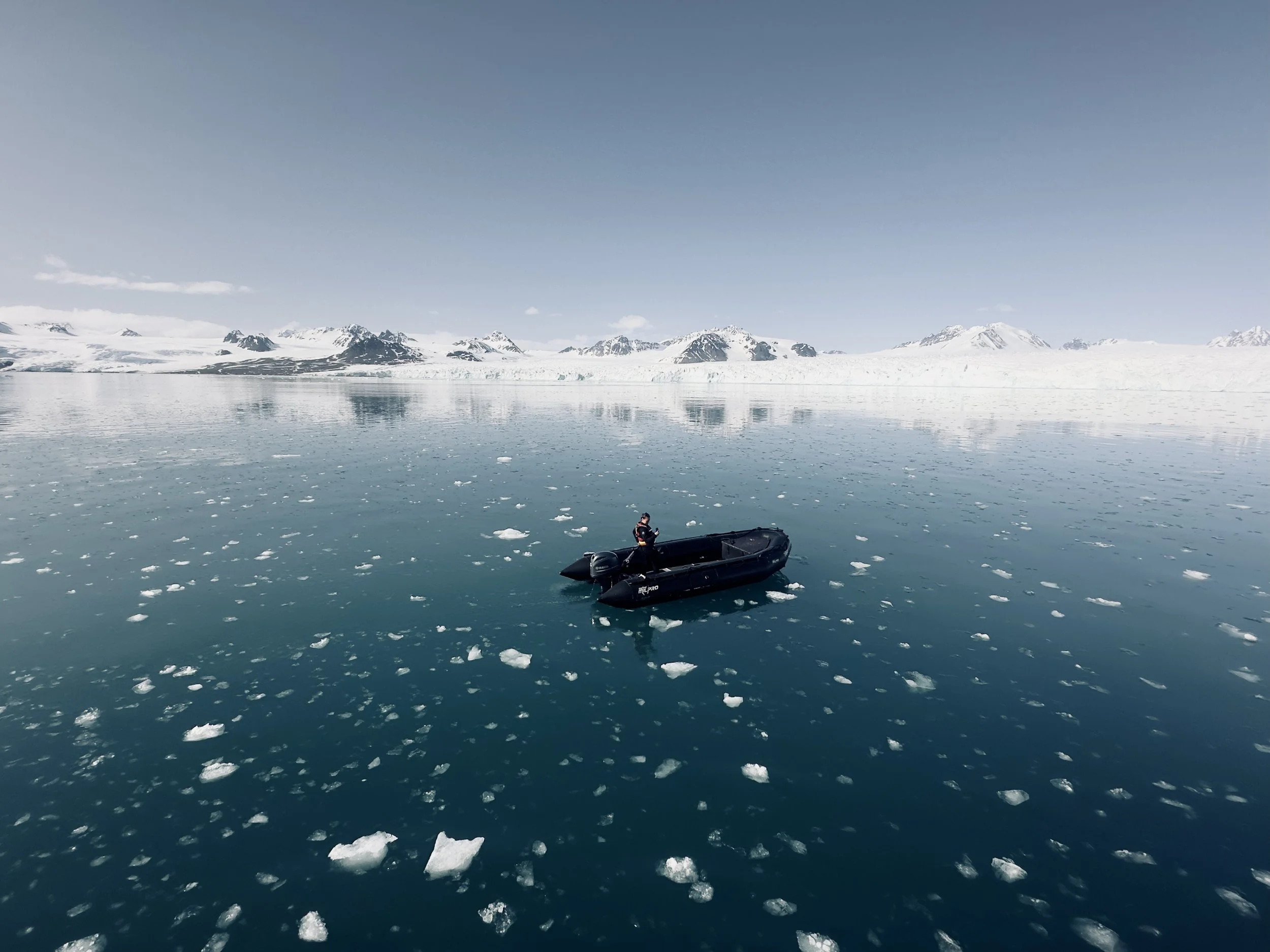 A person in a black inflatable boat on icy waters with snow-covered mountains in the background